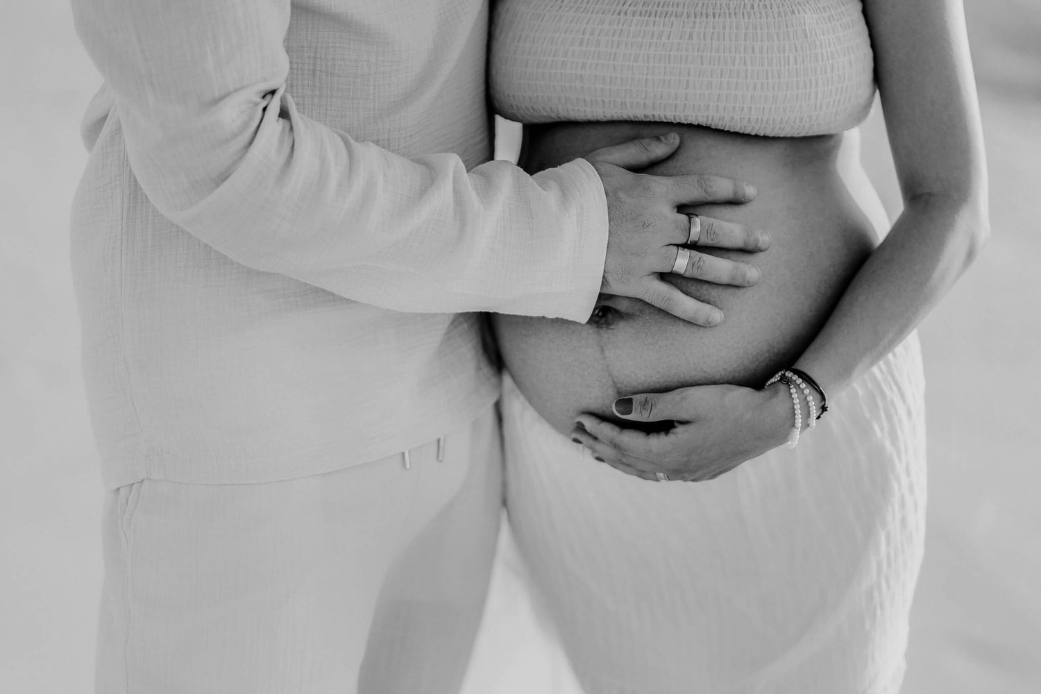 Intimate black and white photo showing hands gently cradling a pregnant belly.