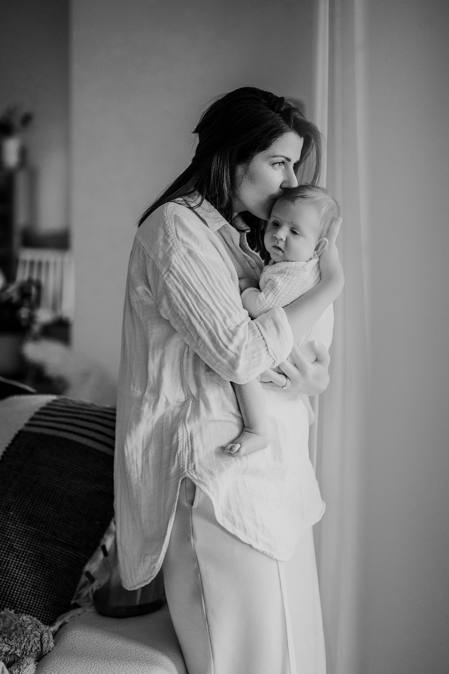 Intimate black and white portrait of tender moment between parent and infant by window.