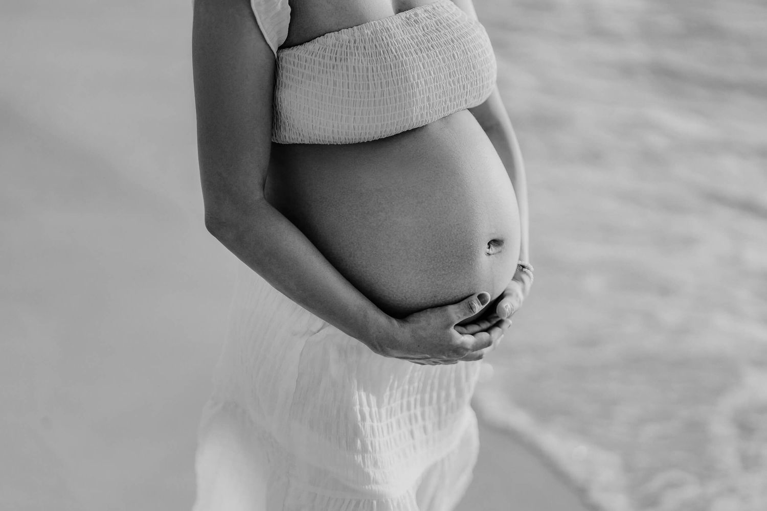 Black and white close-up photo of pregnant belly in soft sweater with hands cradling the bump.
