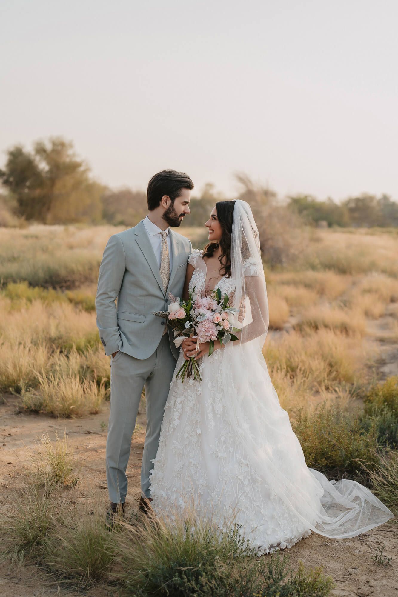 A couple in wedding attire embracing in a golden field during sunset.