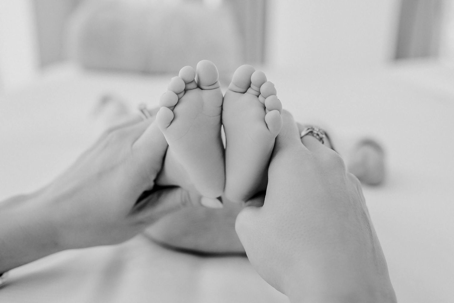 Close up black and white photo of hands holding tiny baby feet.