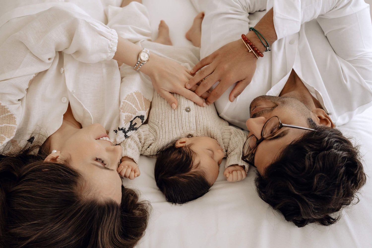 Family cuddles together on white bedding in intimate portrait session.