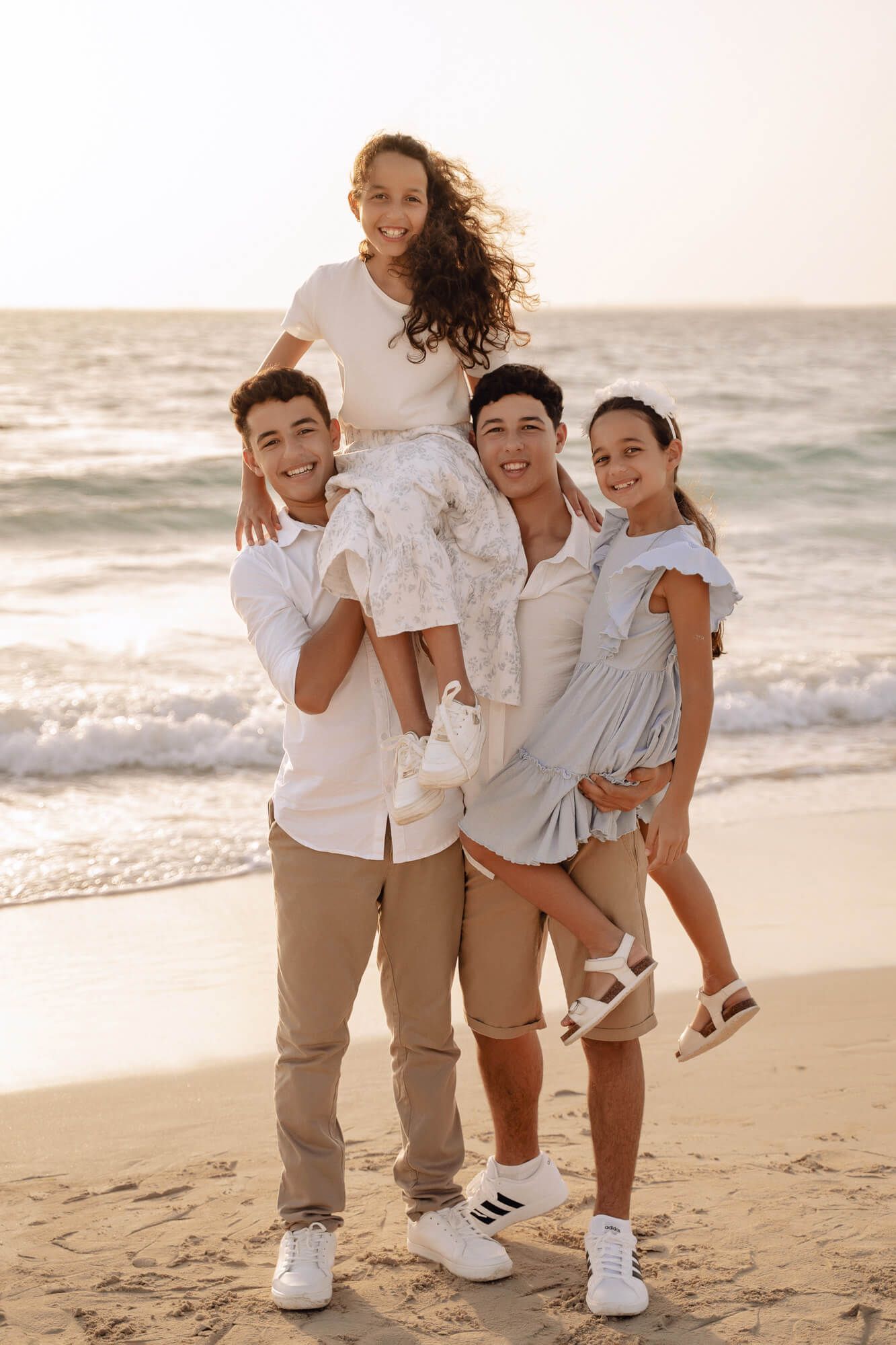 Family of four in coordinating white outfits poses together on beach at sunset.
