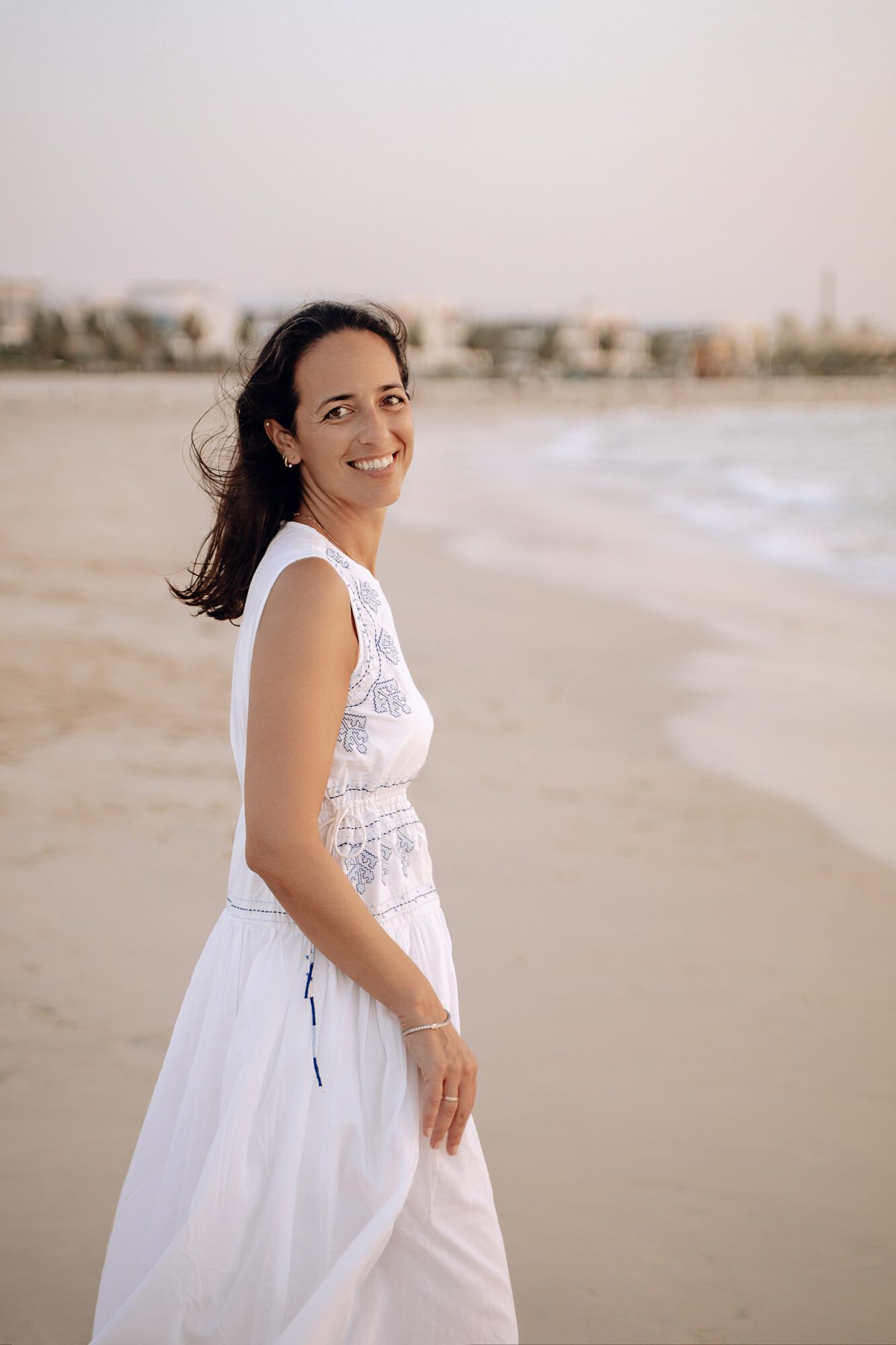 A flowing white embroidered dress catches the breeze on a sunny beach.