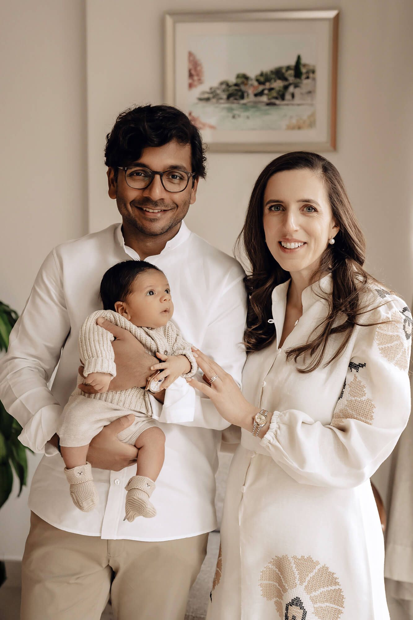 Stylish family portrait in coordinating white outfits poses together against neutral wall with artwork.