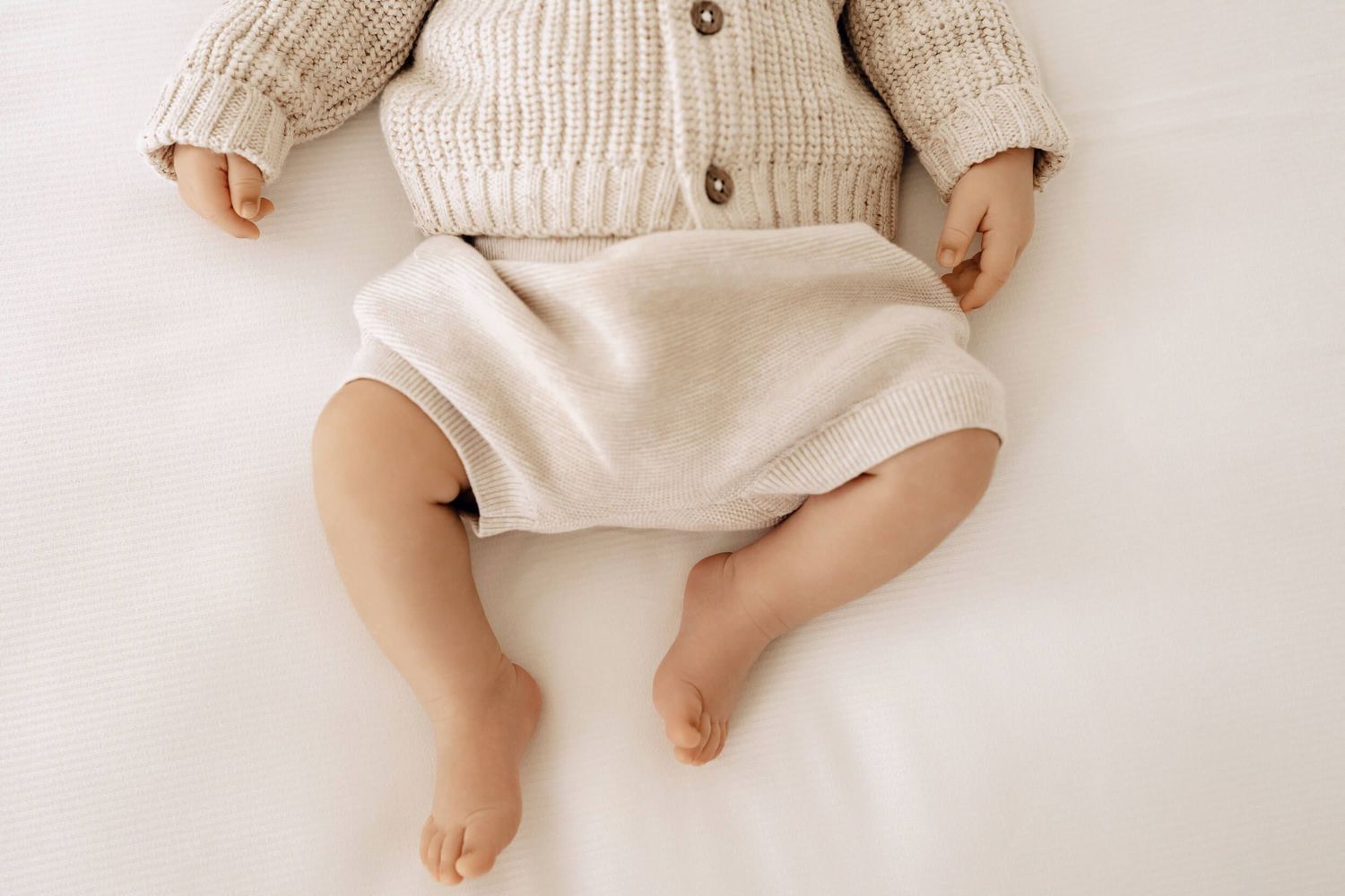 Close-up view of baby's legs wearing a knit cardigan and light-colored shorts.