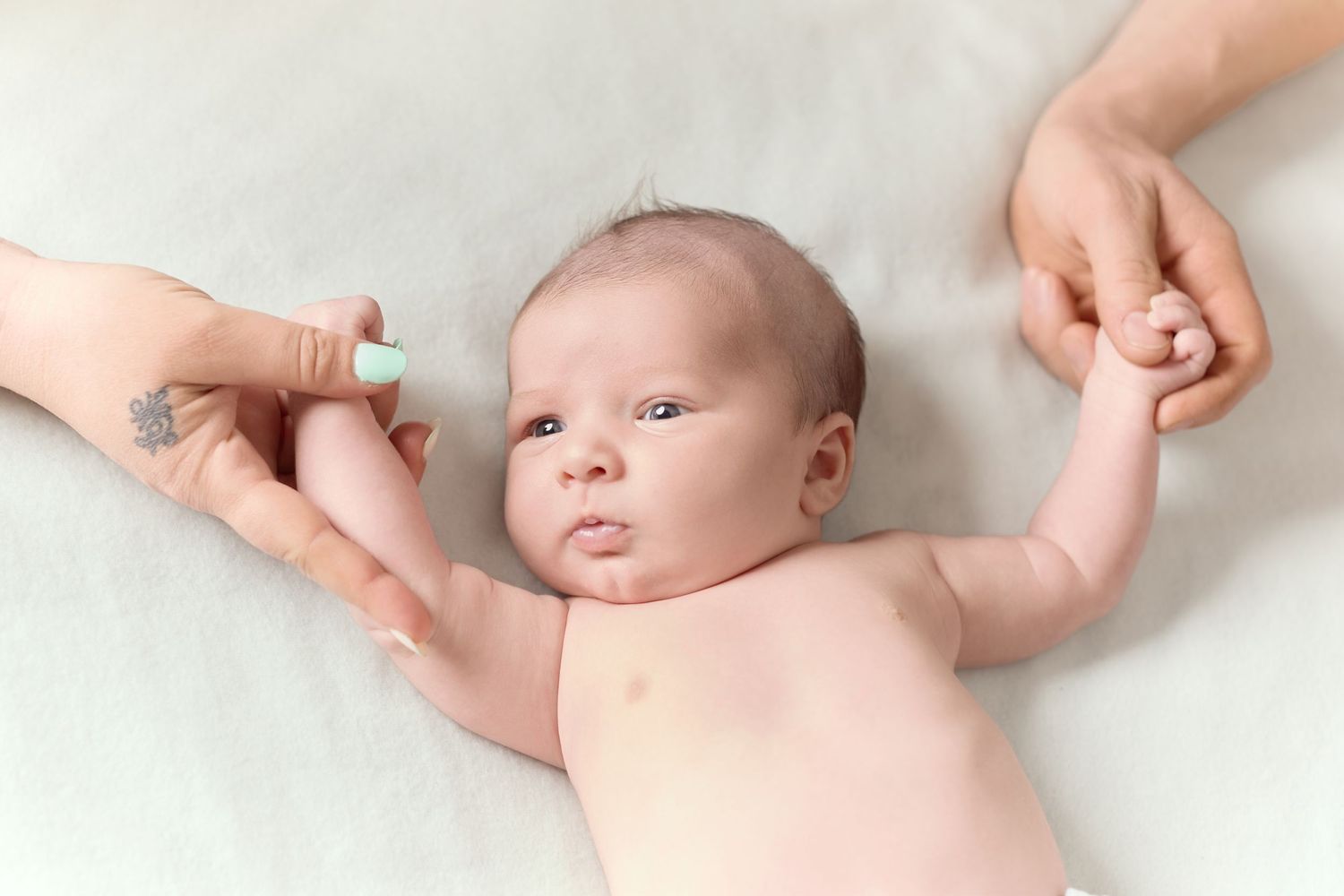 Séance photo naissance à domicile, bébé allongé tenant la main de ses parents – Paul-Victor Photographies.