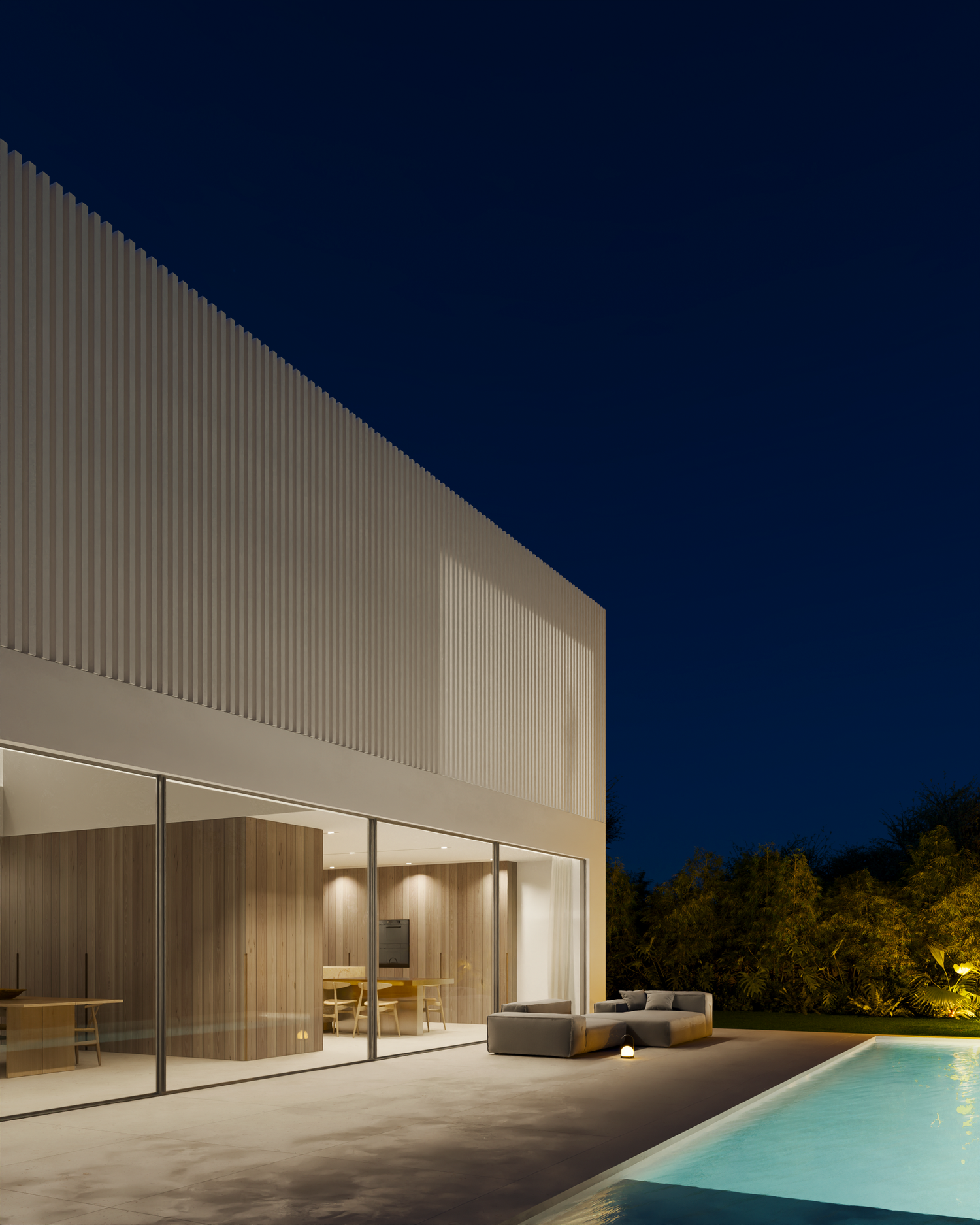 Modern minimalist villa with illuminated infinity pool and glass walls glowing at dusk against a deep blue sky.