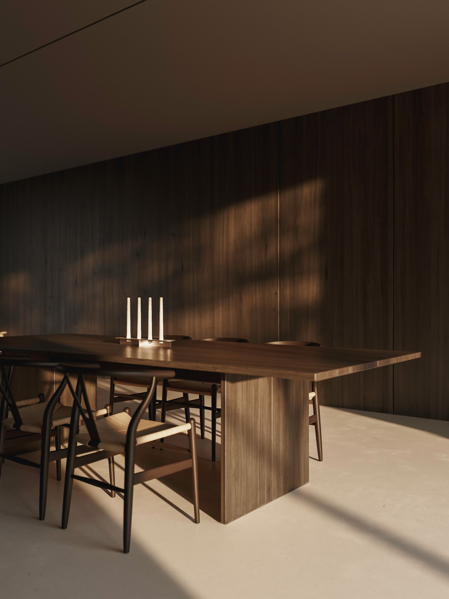 Minimalist dining setup with wooden table, black chairs and white candles against dark wood paneled wall in moody lighting.