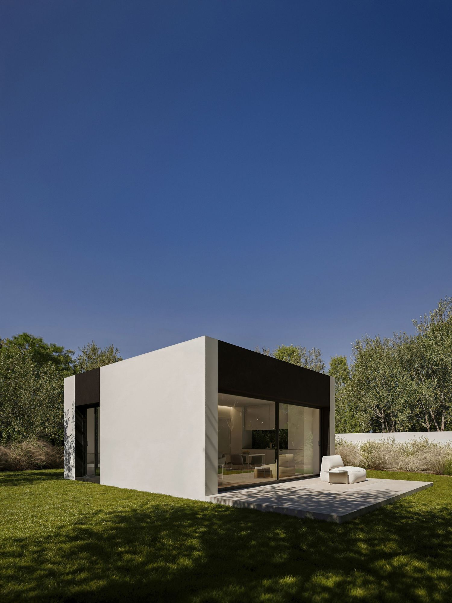 Sleek modern white architectural structure with glass windows set against blue sky and green grass hillside.