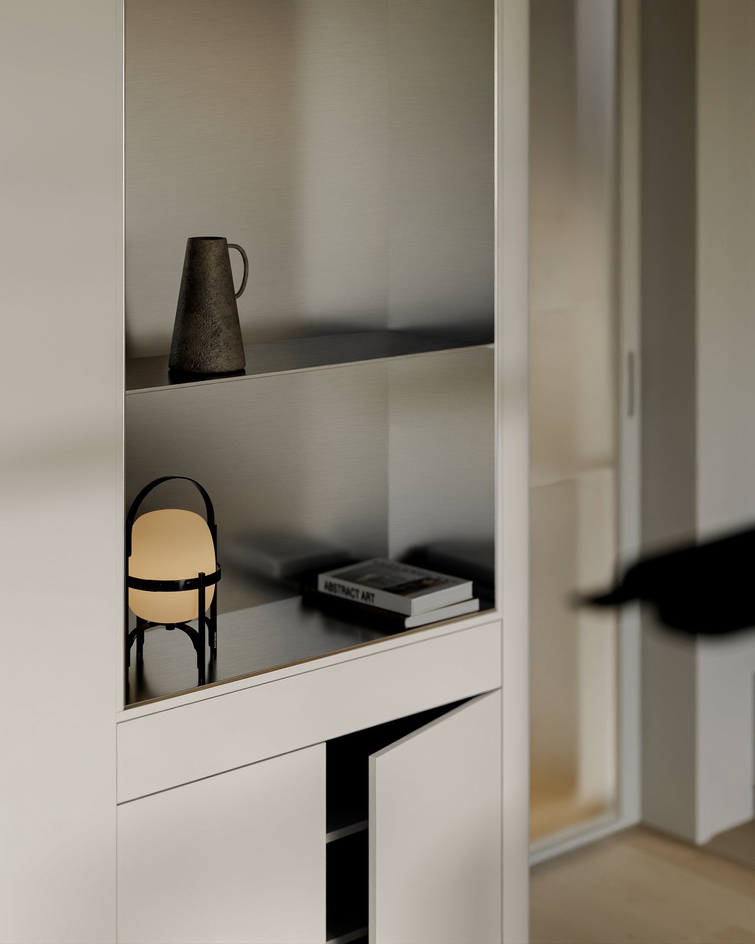 Minimalist white built-in shelving unit displaying a ceramic jug, small lamp, and books in a modern interior.