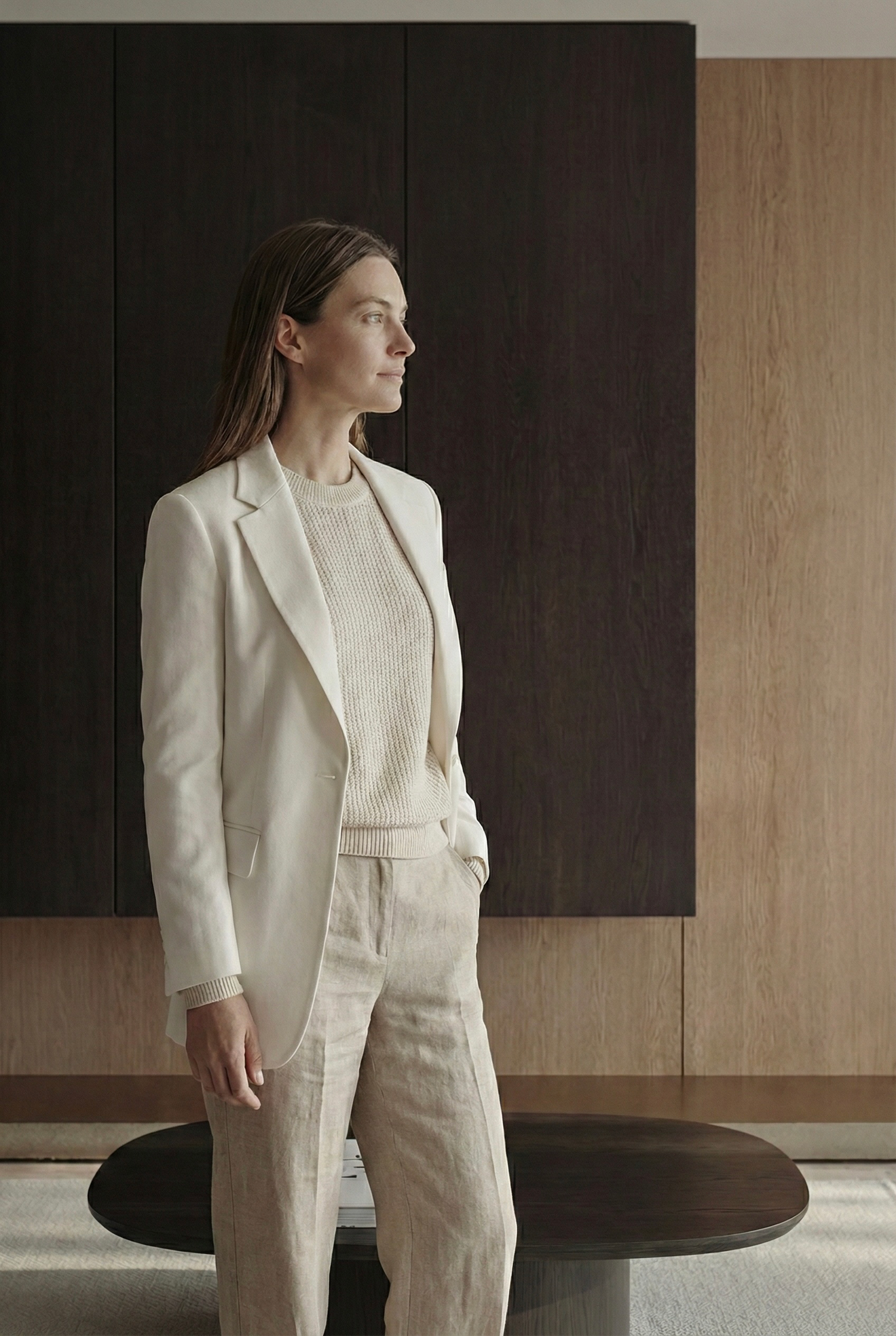 A model poses in a white tailored blazer and matching pants against a minimalist interior with dark accent walls.
