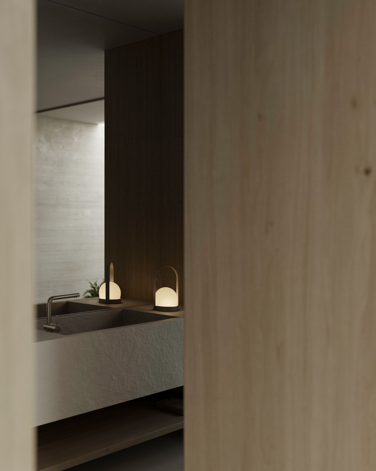 Minimalist bathroom interior with wooden wall panel and two small dome lamps illuminating a dark stone countertop.