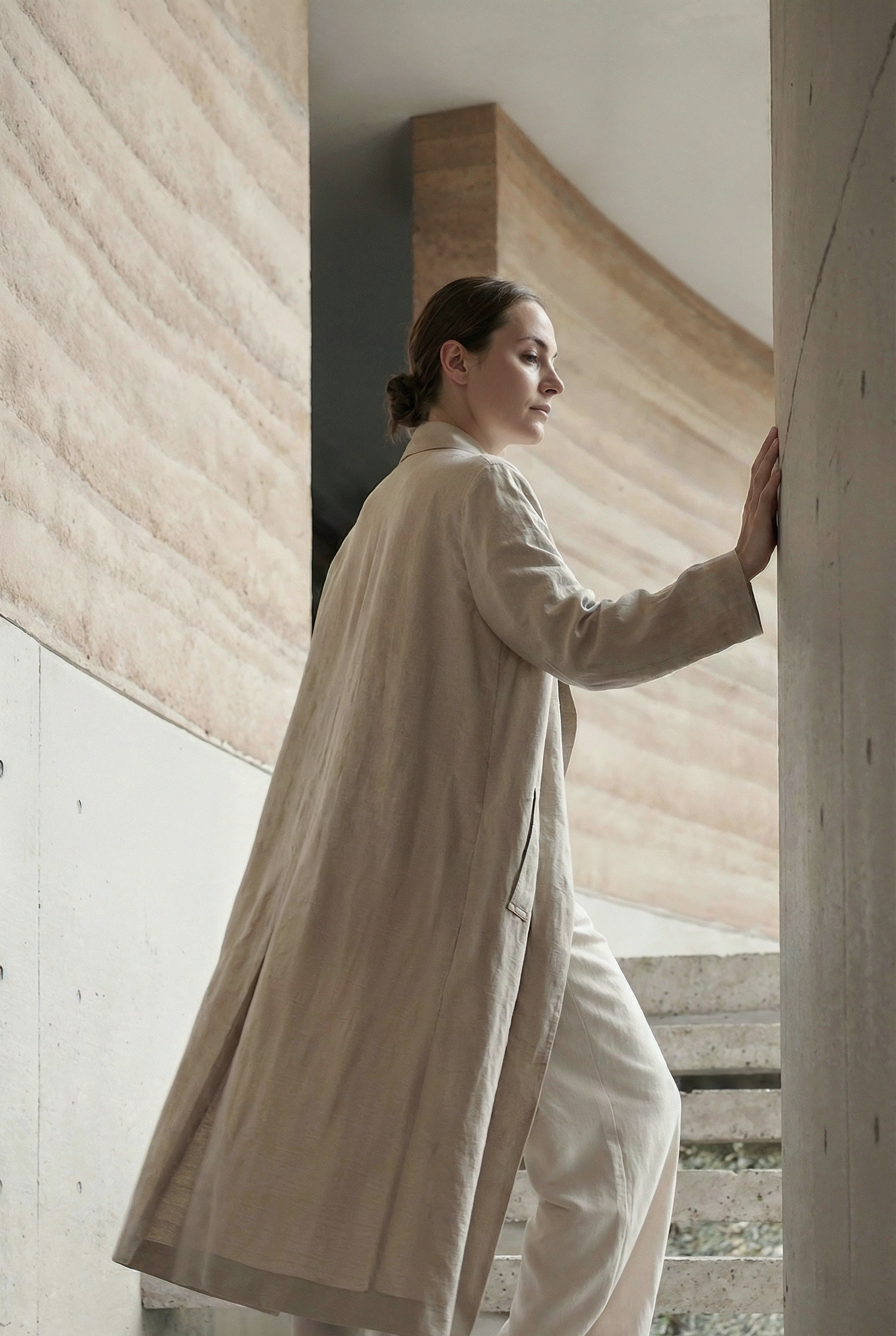 A person in a white oversized blazer poses against a concrete wall in a minimalist fashion photoshoot.
