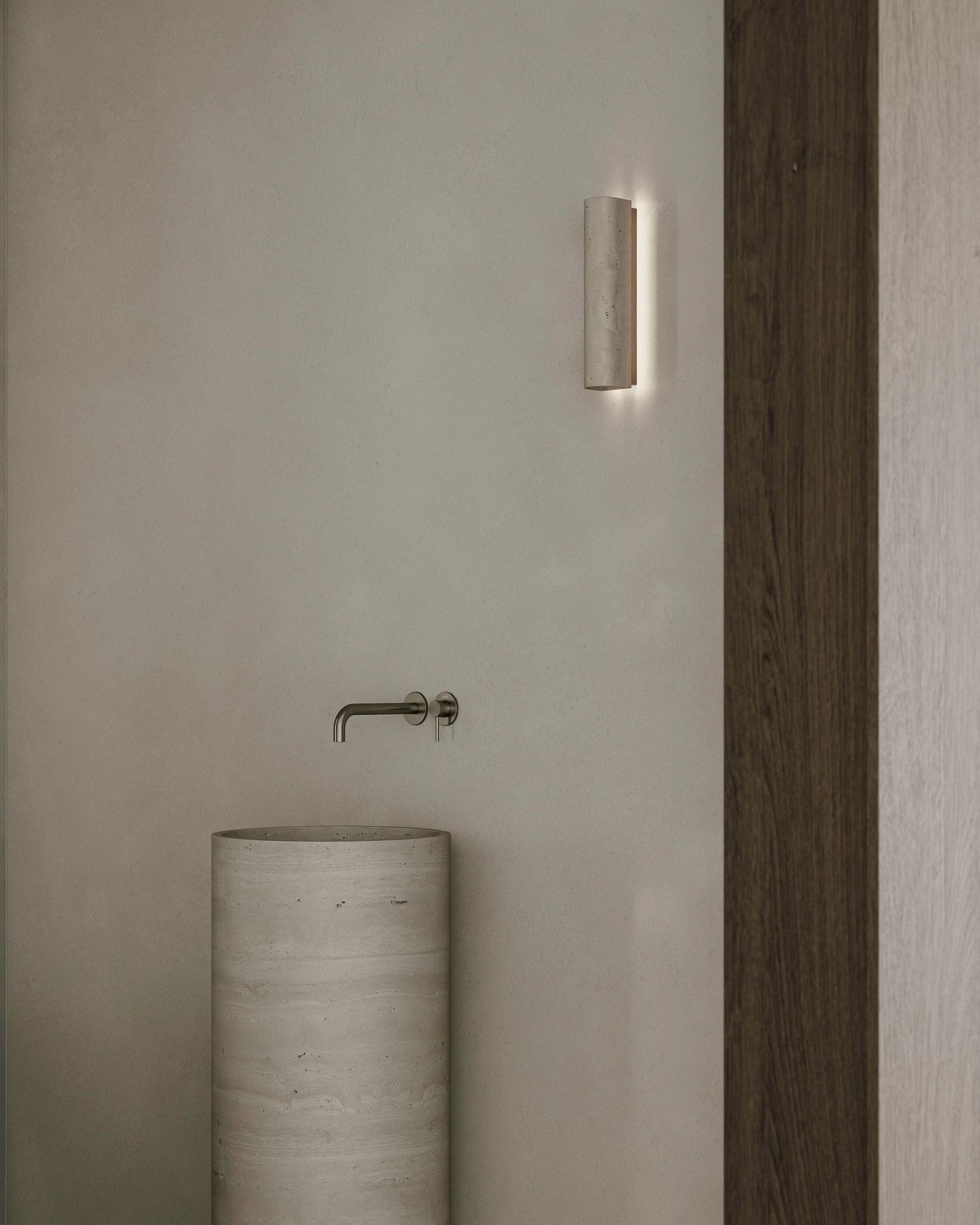 Minimalist bathroom interior with cylindrical pedestal sink, wall-mounted faucet and modern sconce light fixture.