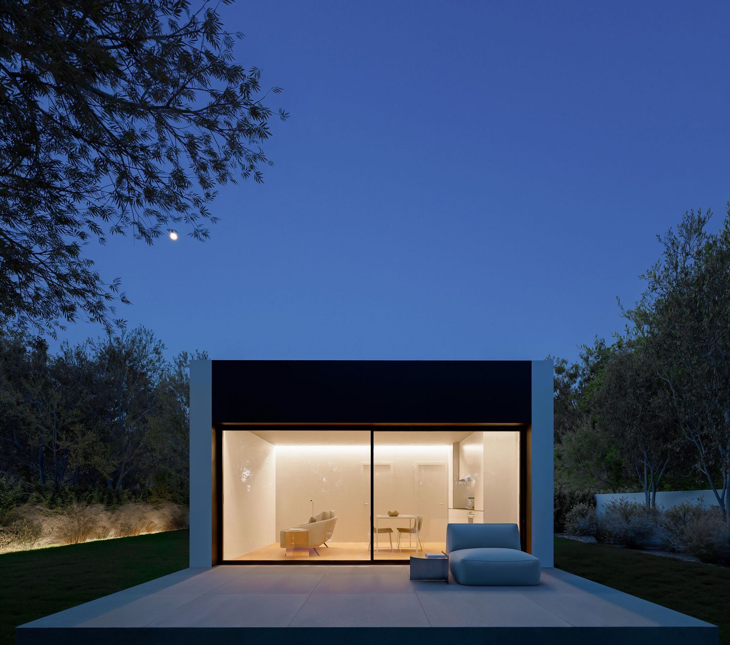Modern minimalist home glows from within at twilight, featuring floor-to-ceiling glass windows and sleek architectural lines.