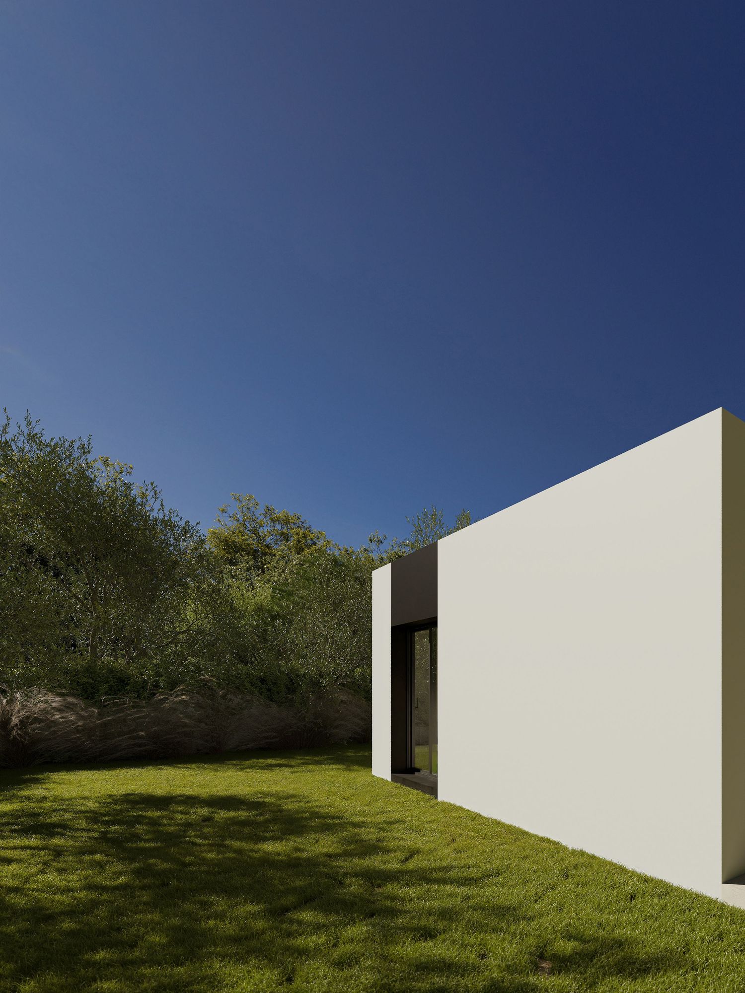 A sequence of minimalist white walls placed on a grassy hillside against a bright blue sky creates a striking modern landscape.