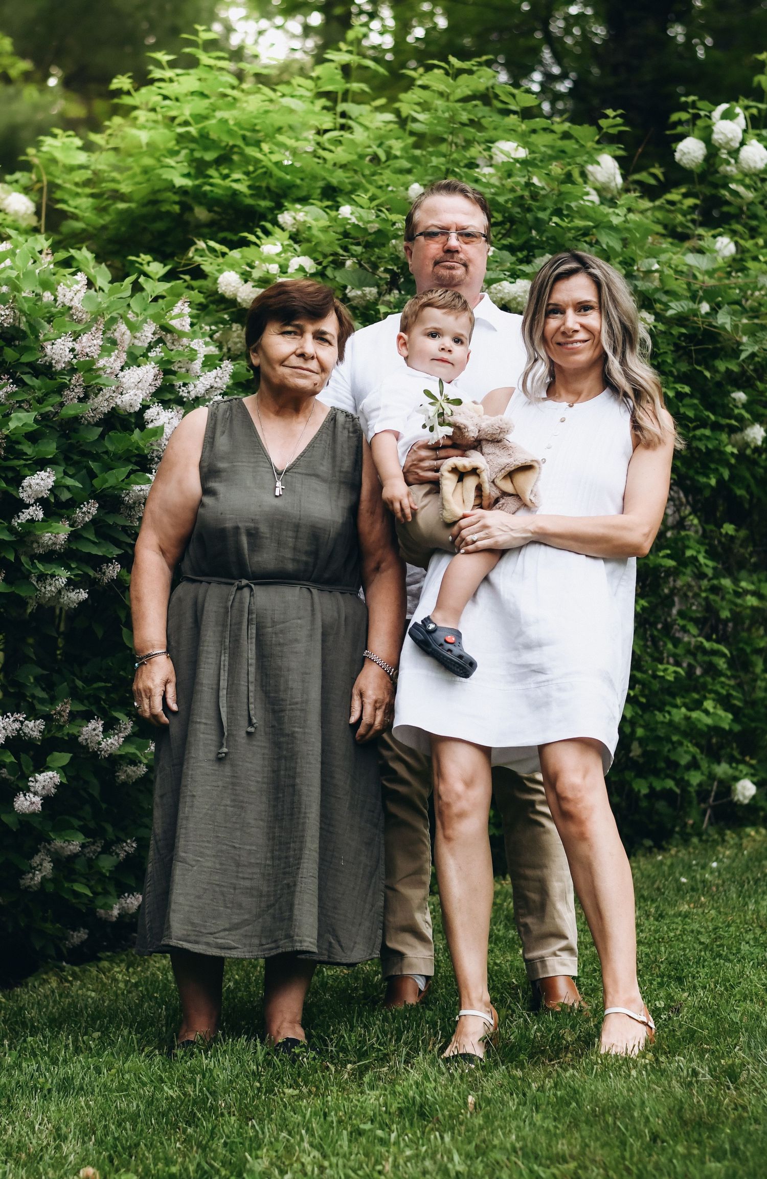 Family group posing together on grass with lilac bushes in the background.
