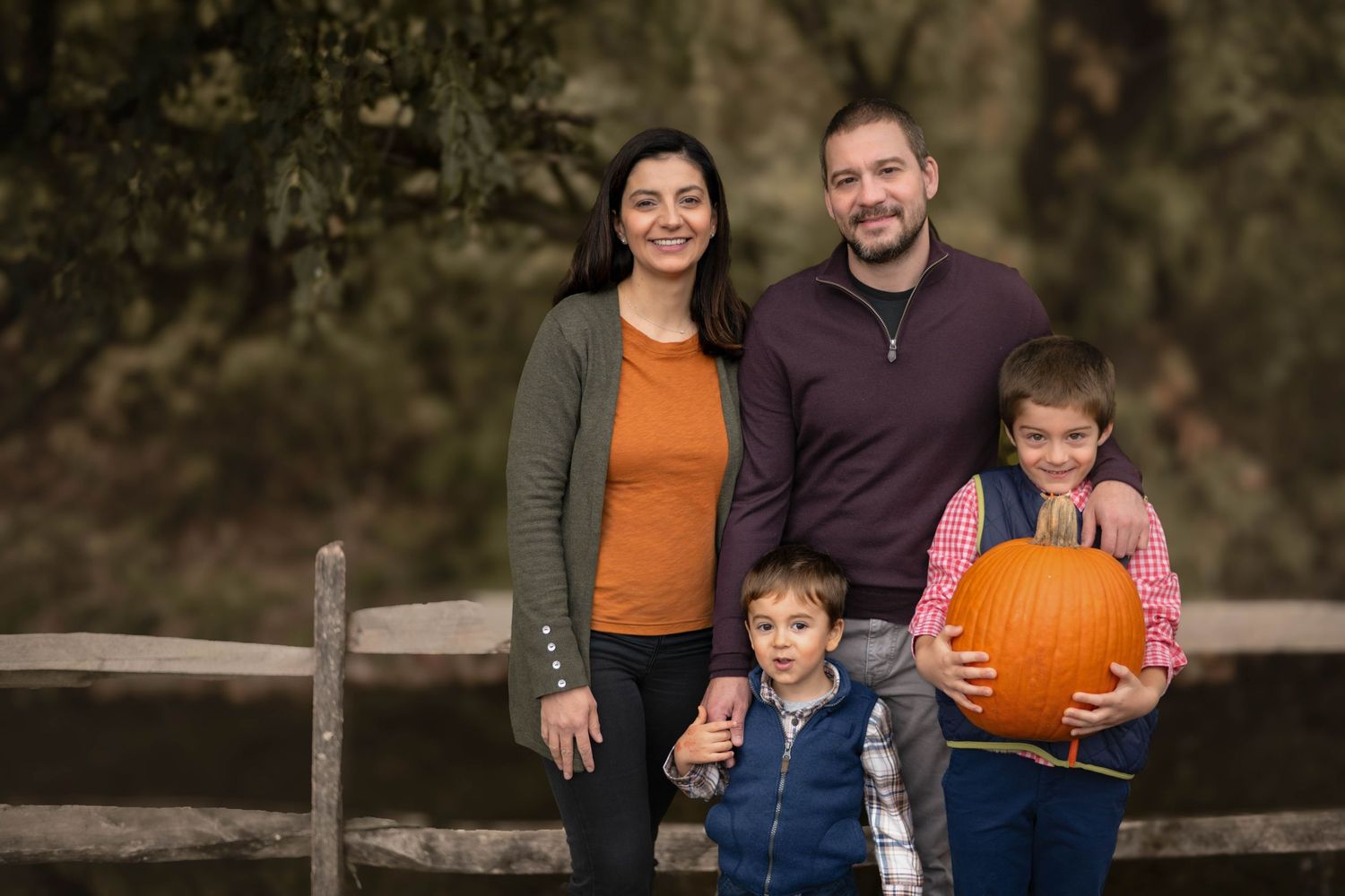 Family of four posing with pumpkins during a fall family photography session on the Main Line, PA.