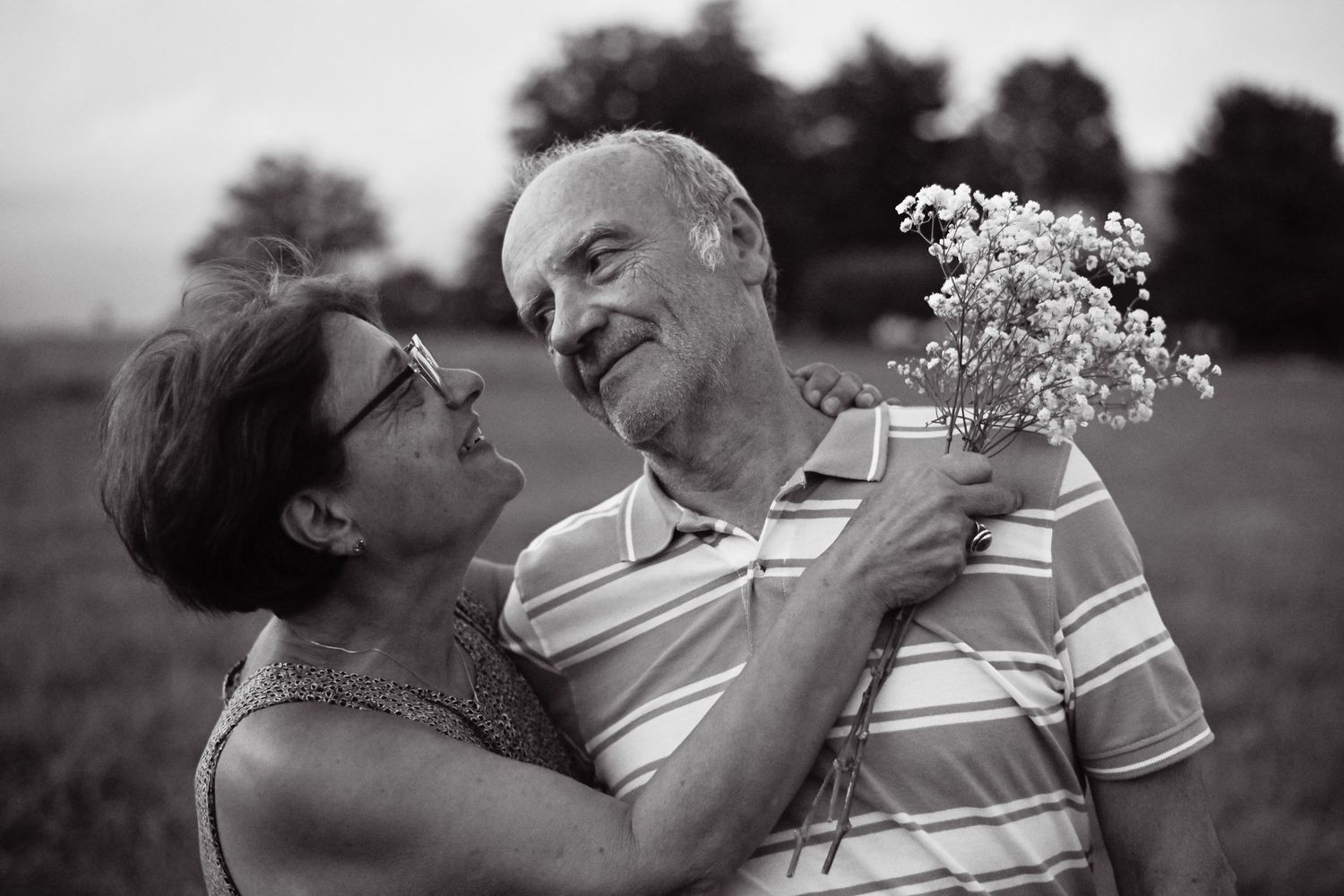 Black and white photo of a couple sharing tender moments in a field.