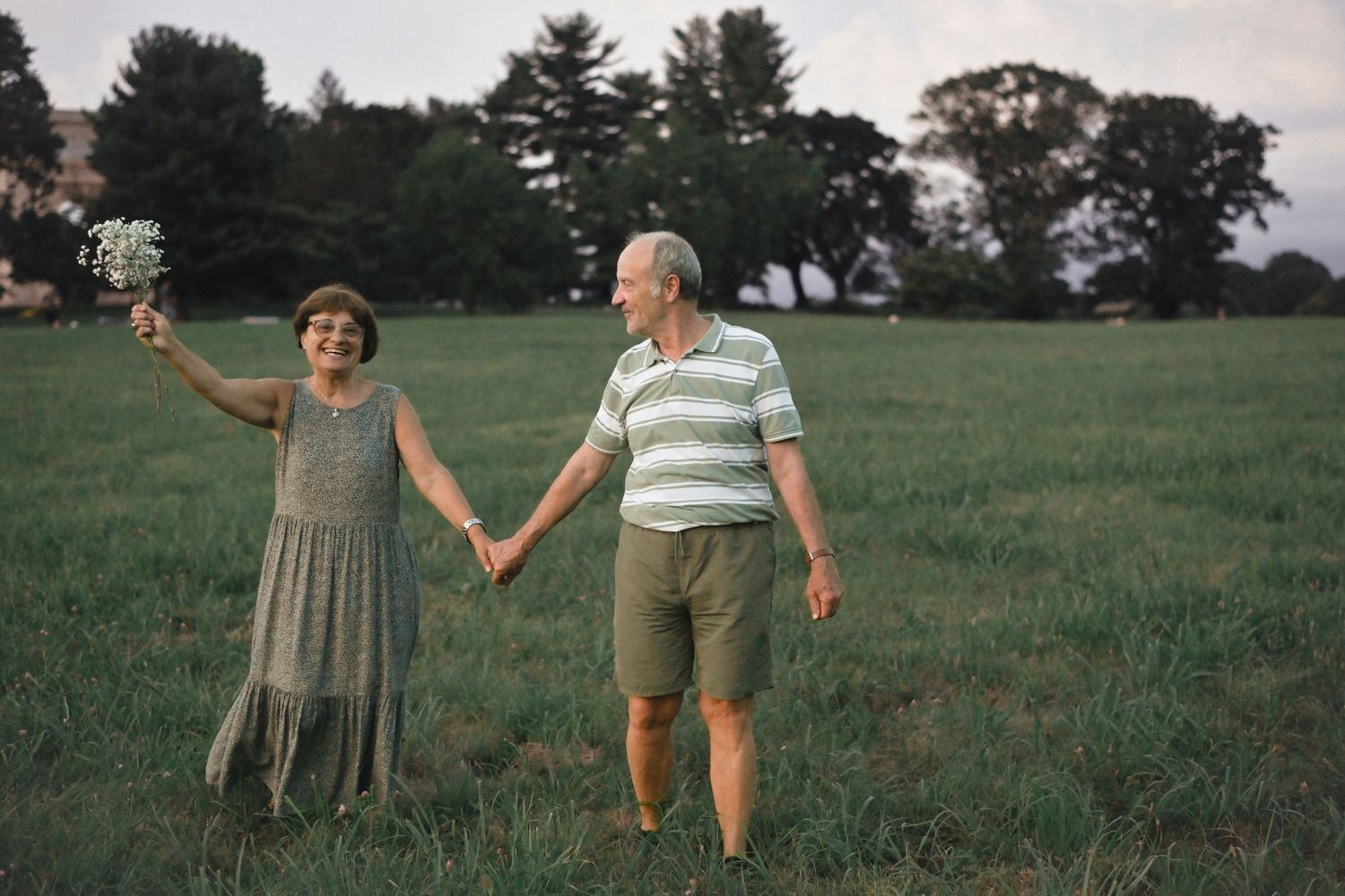 Couple enjoying a playful moment together in an open grassy field with trees in the background.