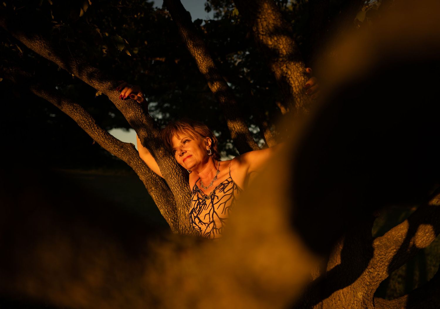 Artistic nighttime portrait with dramatic orange lighting through tree branches.