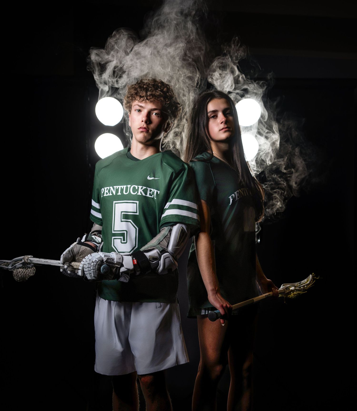 Two Pentucket lacrosse players posing dramatically against a dark smoky background during their senior studio glam session on the Main Line.