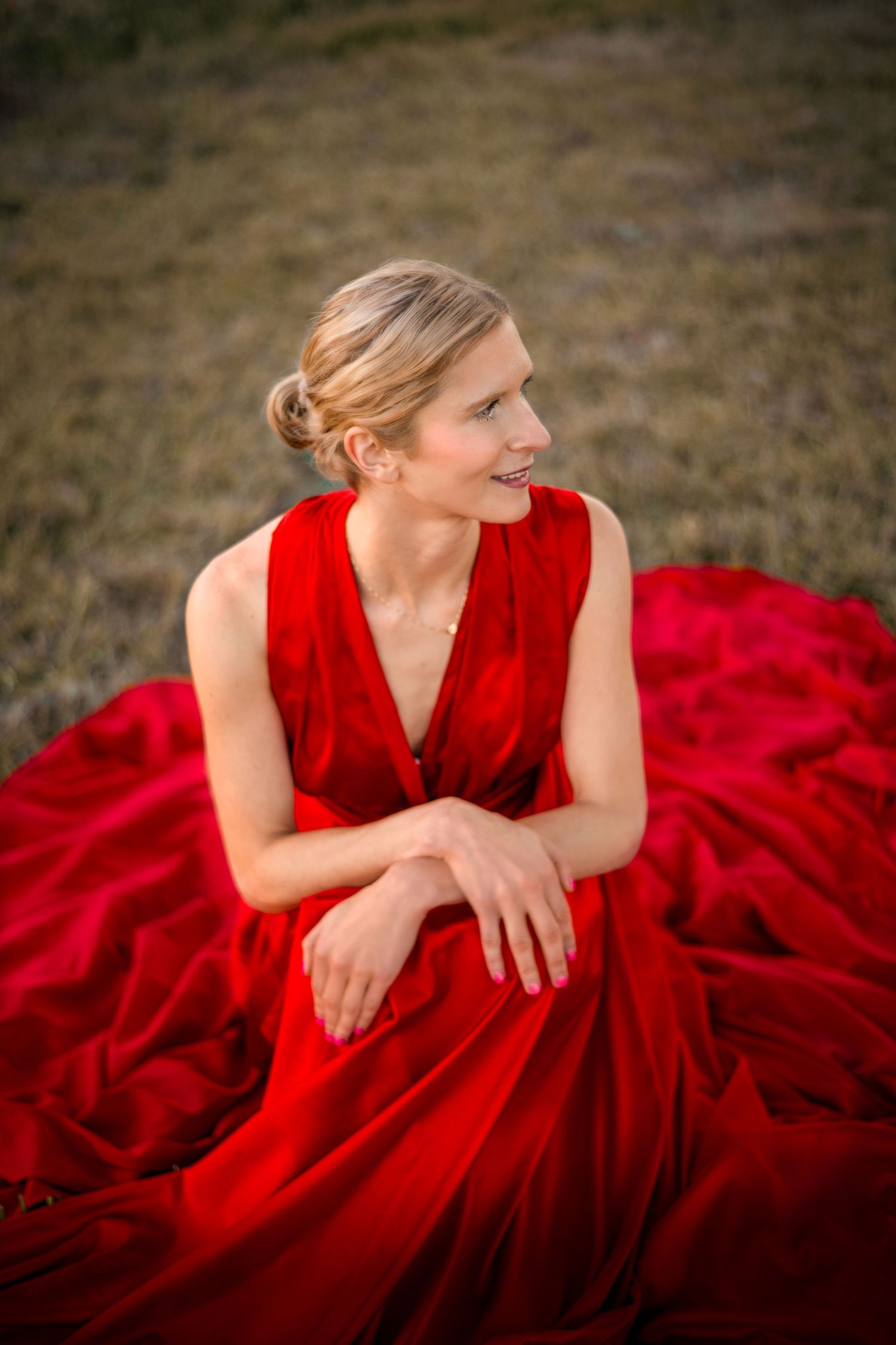 Elegant portrait of woman in vibrant red gown sprawled on grass.