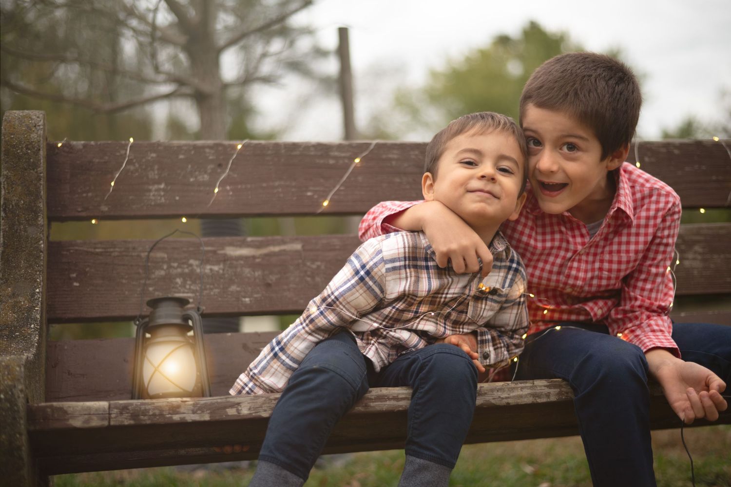 Two young boys laugh together while sitting on a wooden bench outdoors.