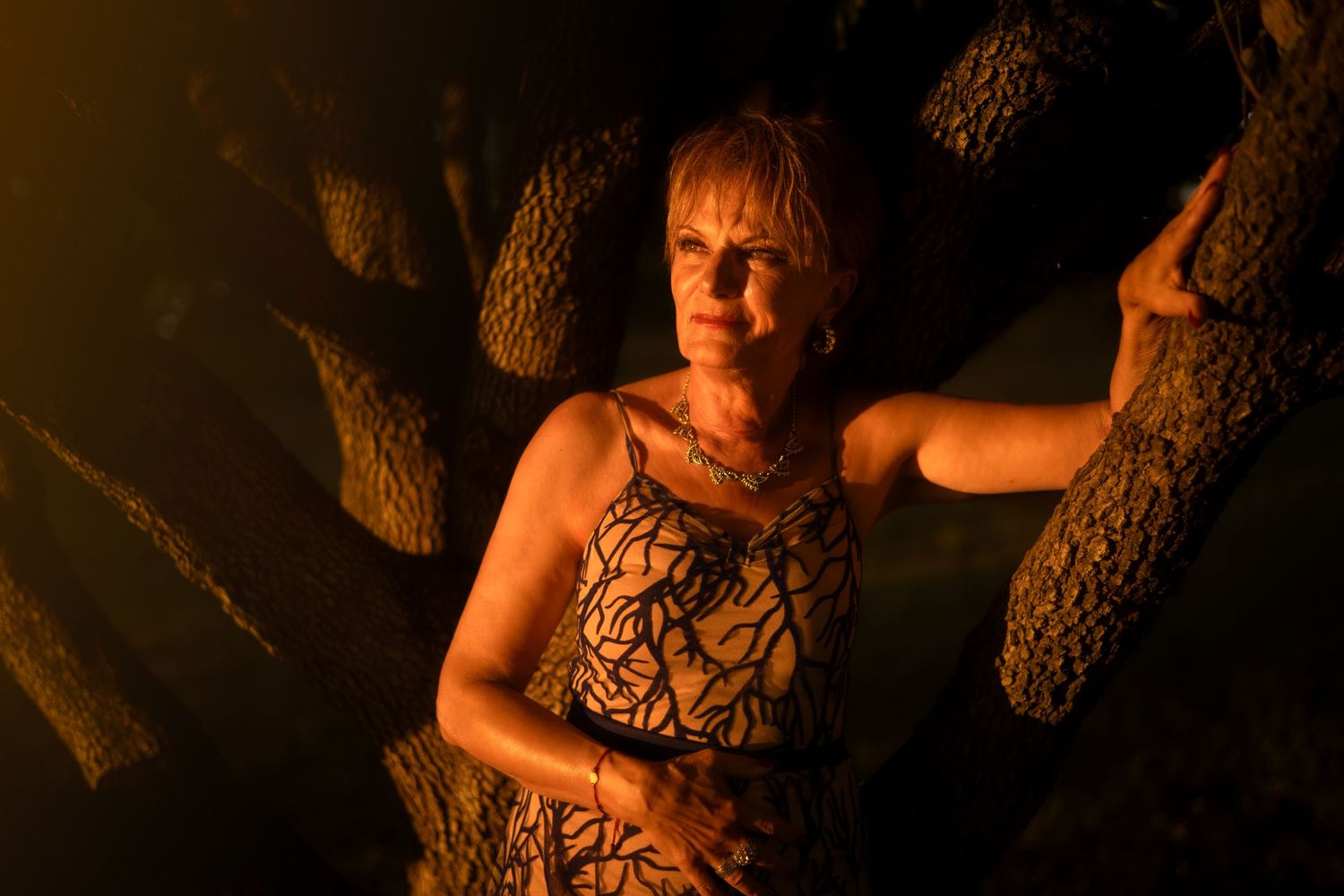 Moody portrait with warm lighting and tree silhouettes at night.