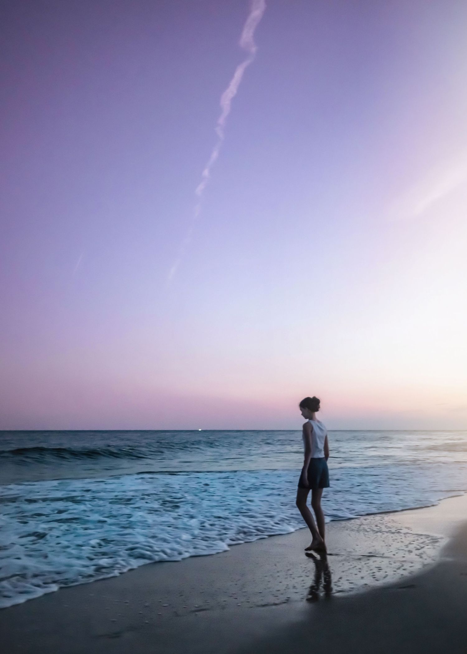 A solitary figure standing at the ocean's edge during twilight with waves rolling in.