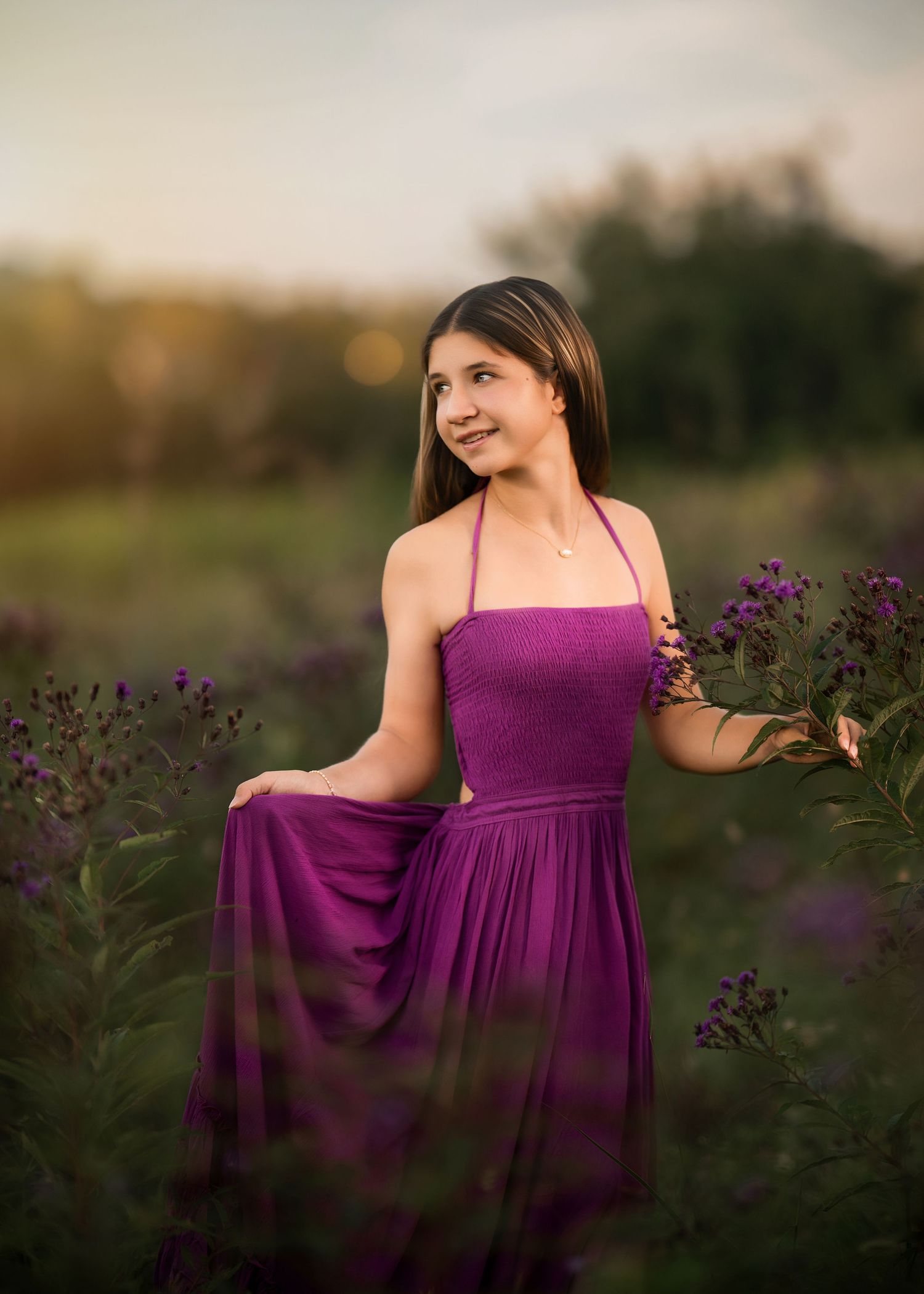 Young woman in purple halter dress standing among wildflowers at golden hour.