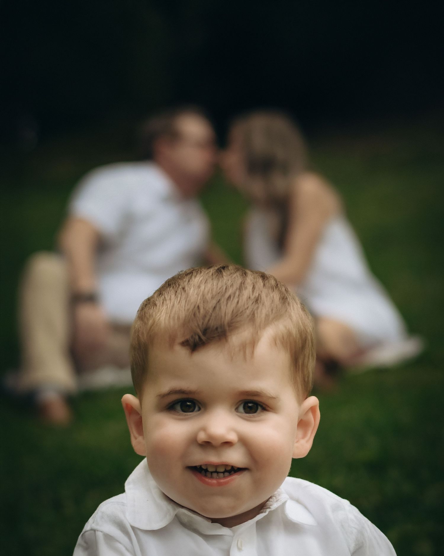 Toddler in white clothing smiling while playing outdoors.