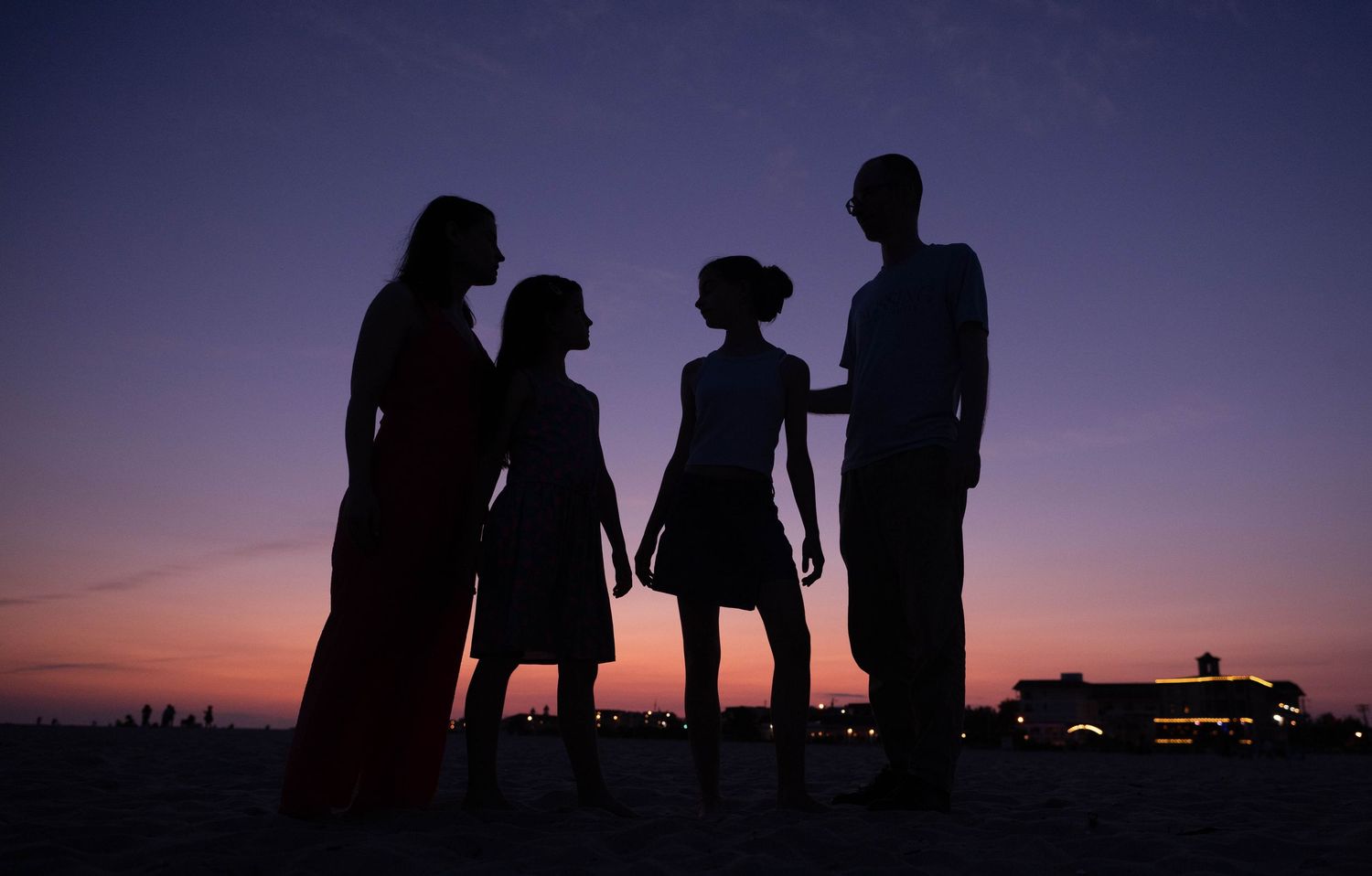 Silhouettes of a family group standing together against a purple sunset sky.