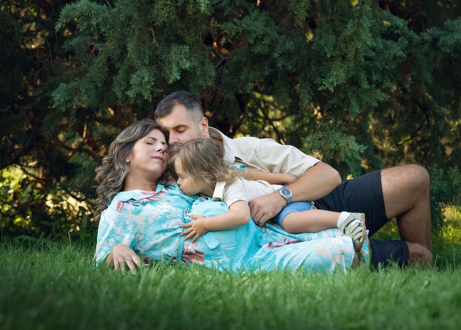 A loving family relaxes on green grass during their family outdoor photo session.