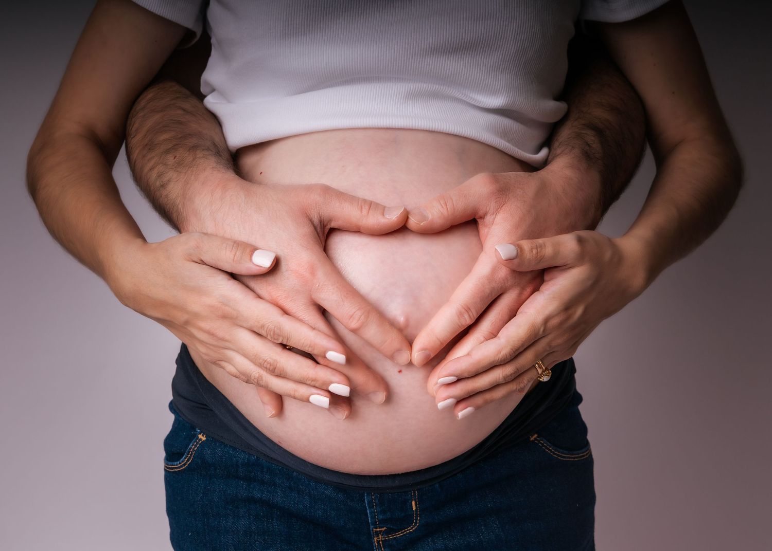 Couple forming a heart shape with hands on pregnant woman's bare belly, maternity love concept.