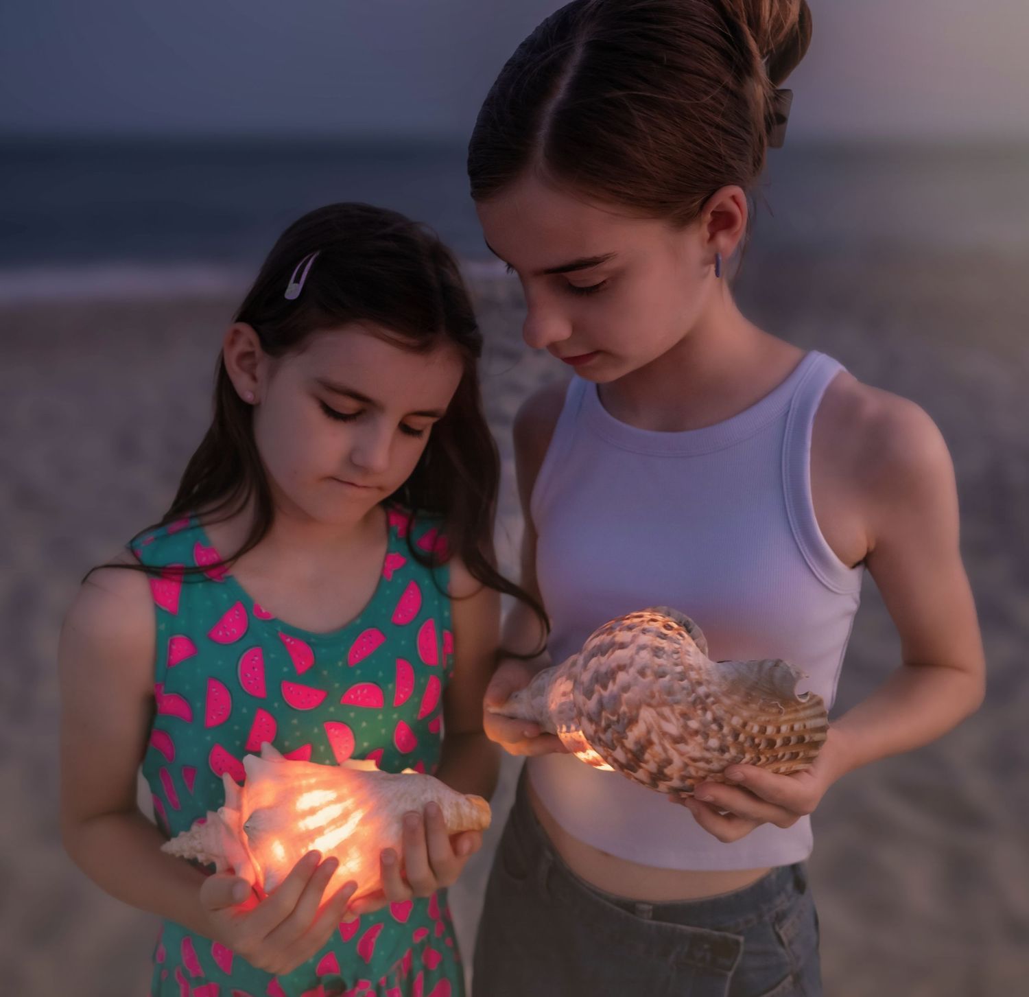 Two figures holding glowing seashells on a beach at dusk.