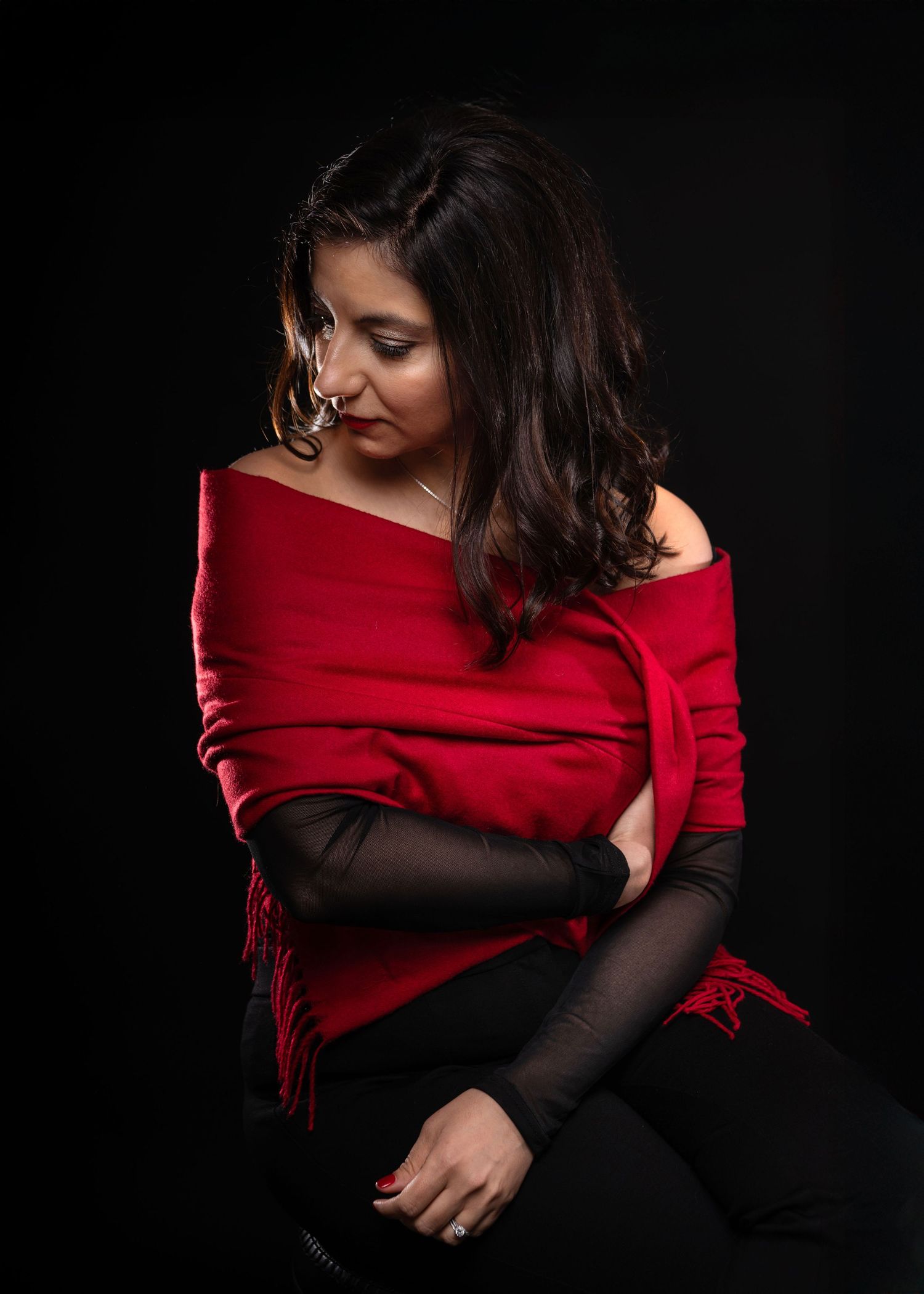 Woman in red off-shoulder wrap and black mesh sleeves poses against dark background.