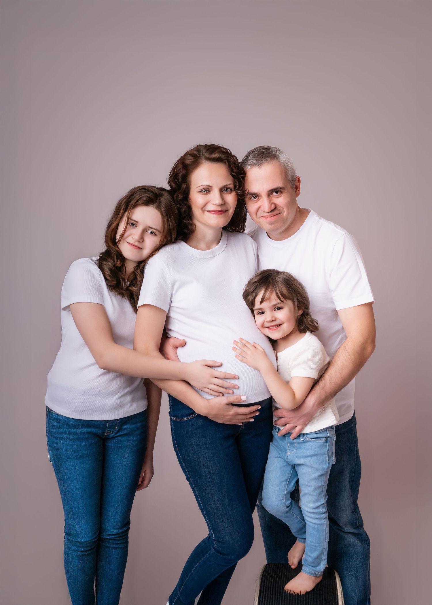 Family maternity photo with pregnant mother, father, teen daughter, and toddler girl in white shirts and jeans.