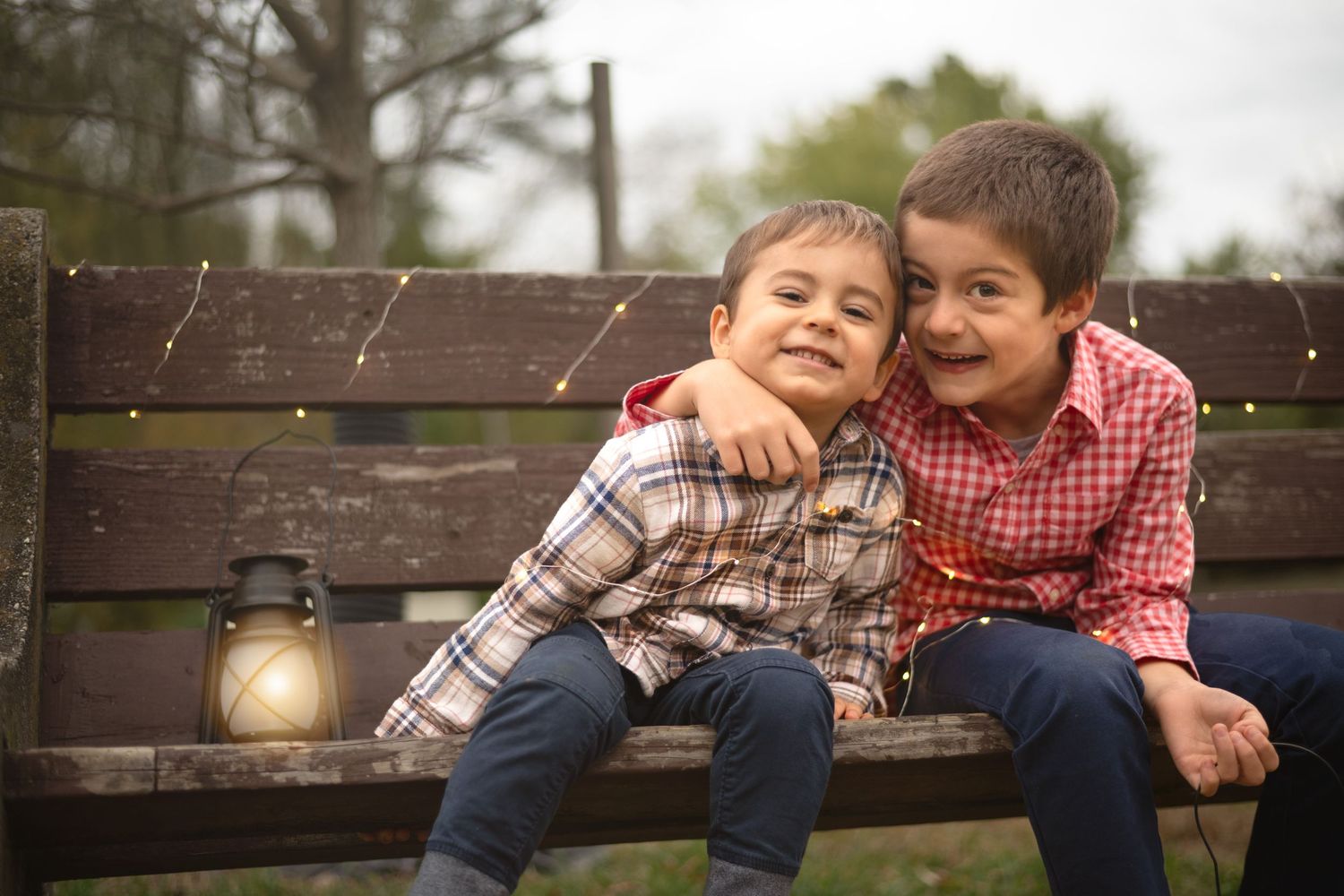 Two boys in casual attire share joyful expressions while relaxing on an outdoor bench.