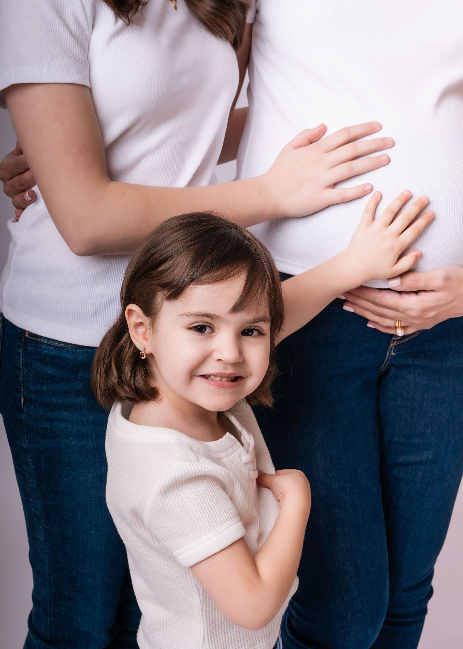 Young girl smiling and touching pregnant woman's belly during a family maternity photo session.