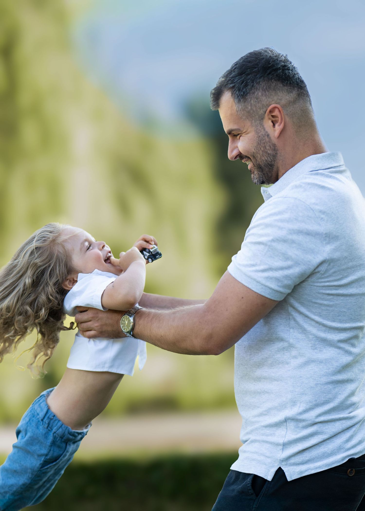 A smiling father lifts his laughing young child sharing a tender moment during their family portrait session.