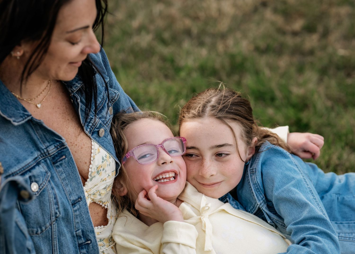 A mother and two daughters sharing a joyful embrace outdoors during their golden hour Mommy & Me portrait session near Wayne, PA.