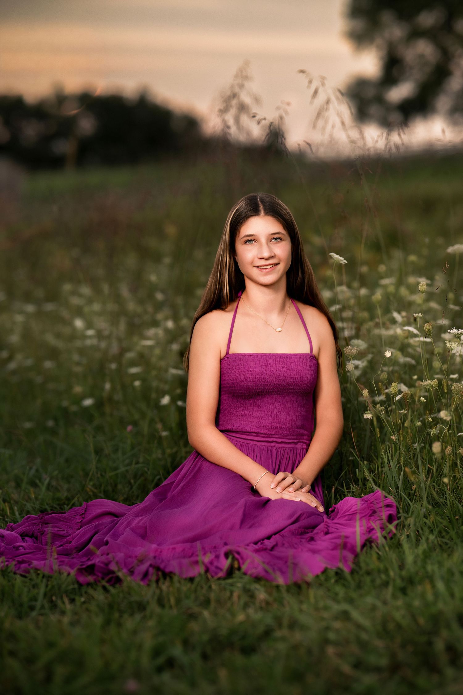 Young woman in purple dress sitting in wildflower field at sunset.