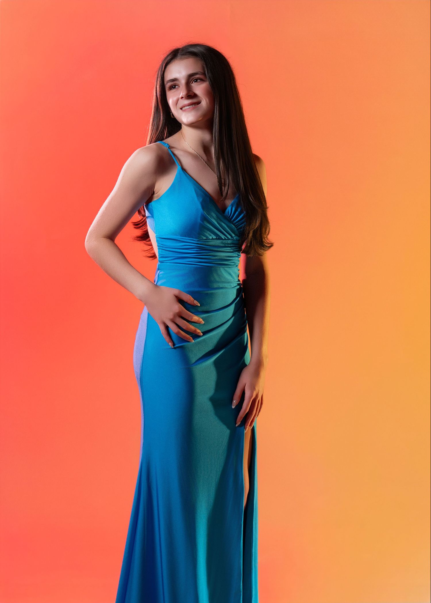 A high school senior in a maxi blue dress posing for a glam portrait with dramatic lighting near Wayne, PA.