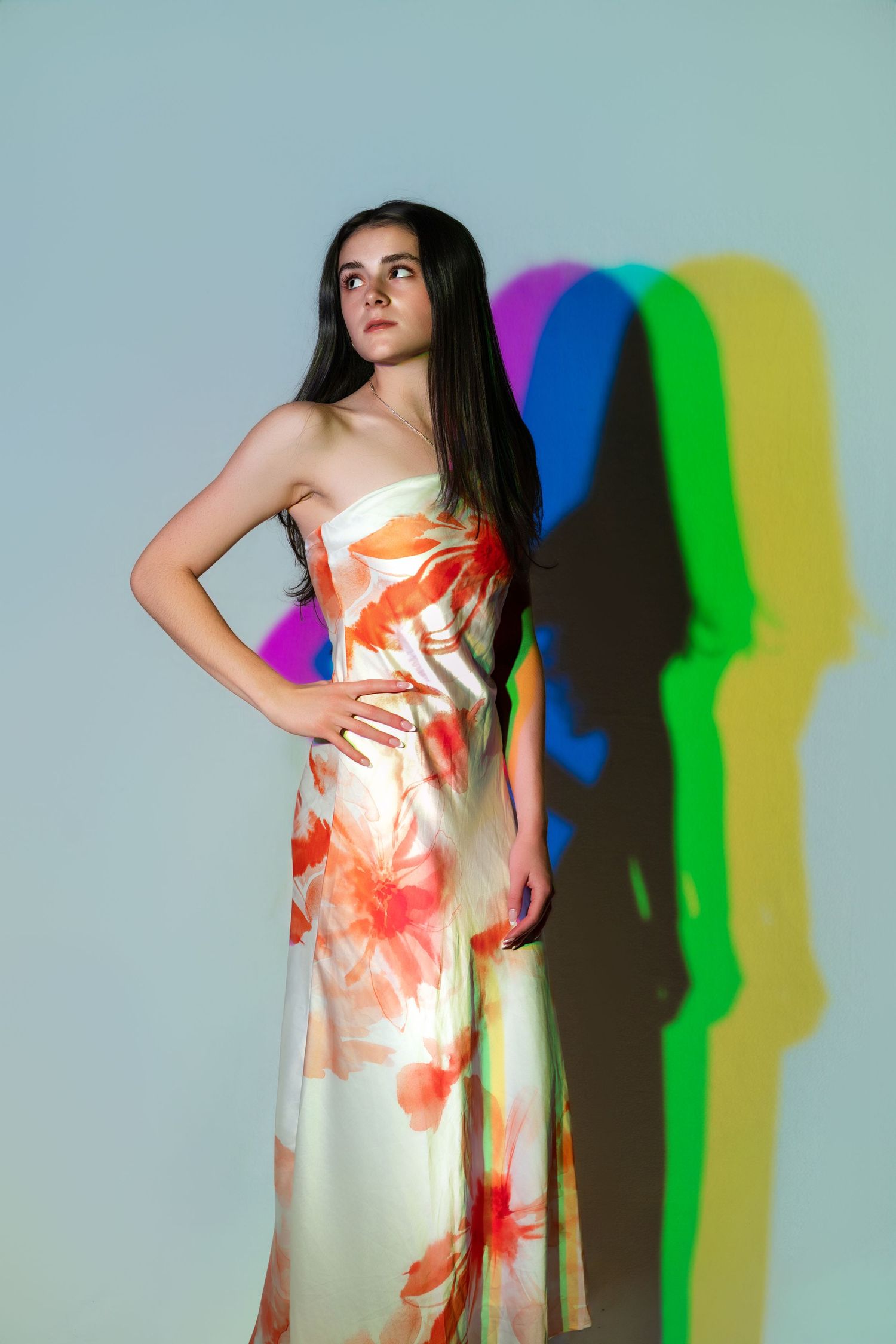 Young woman in floral strapless dress poses against light background with colorful RGB shadows.