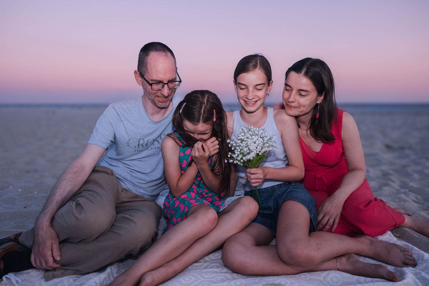 Family relaxing together on sandy beach during sunset with ocean waves in background.