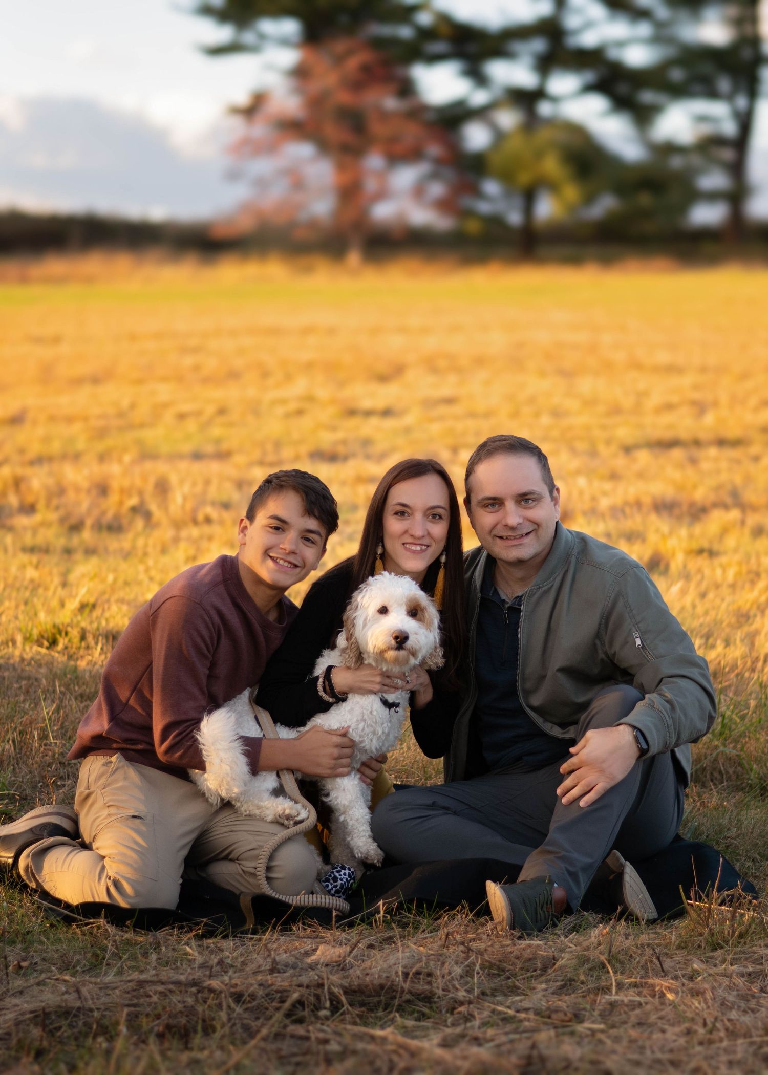 Family portrait with their dog in a golden field at sunset on the Main Line, PA.