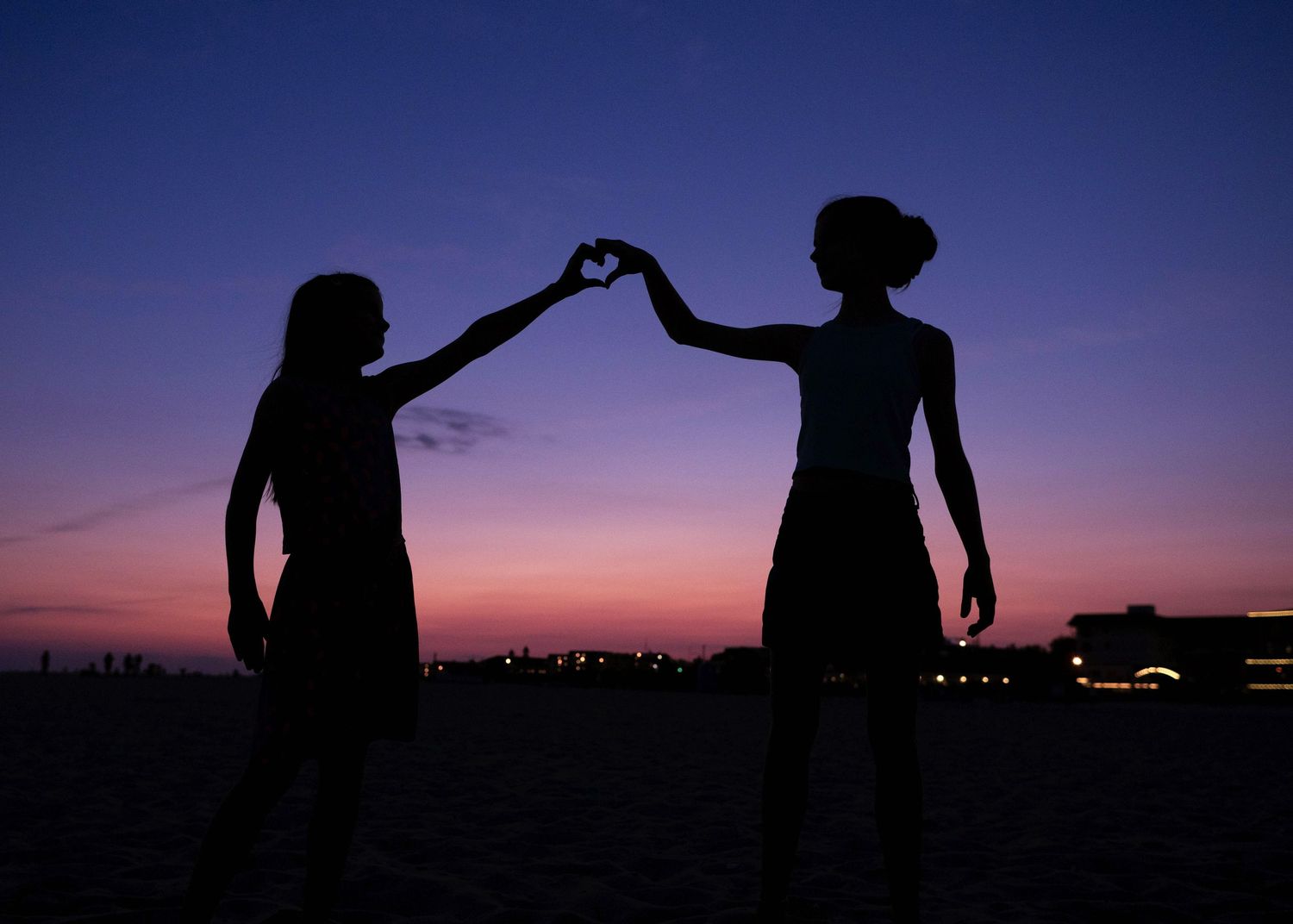 Two silhouettes forming a heart shape with their arms against a vibrant sunset sky.