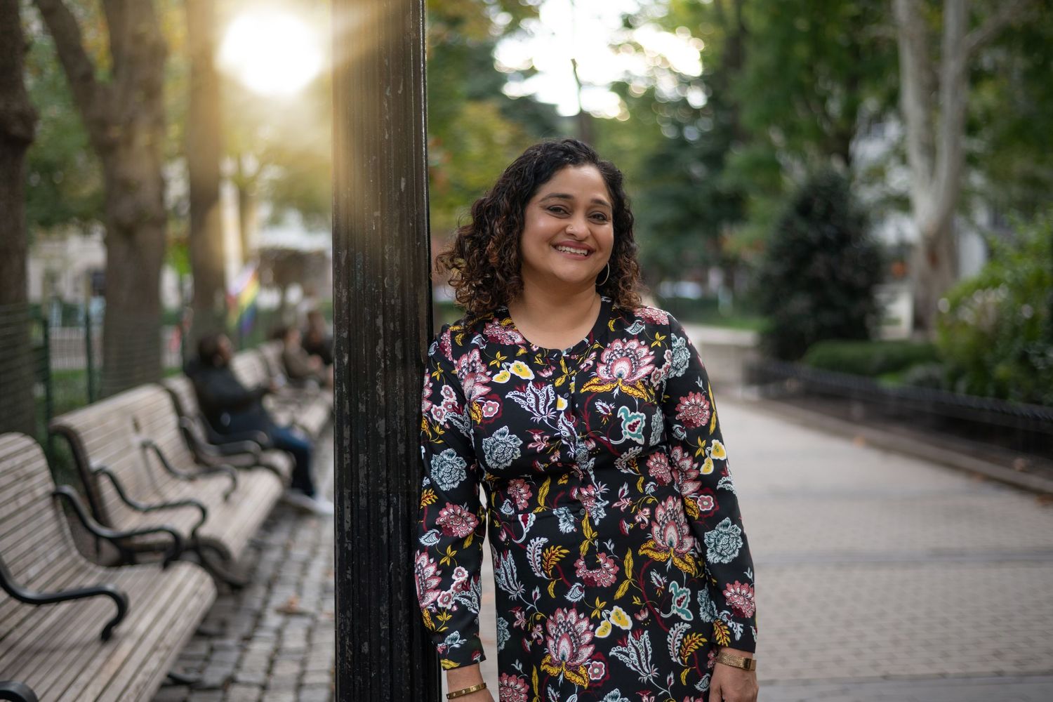 Person in floral dress walking through a park with benches at golden hour.